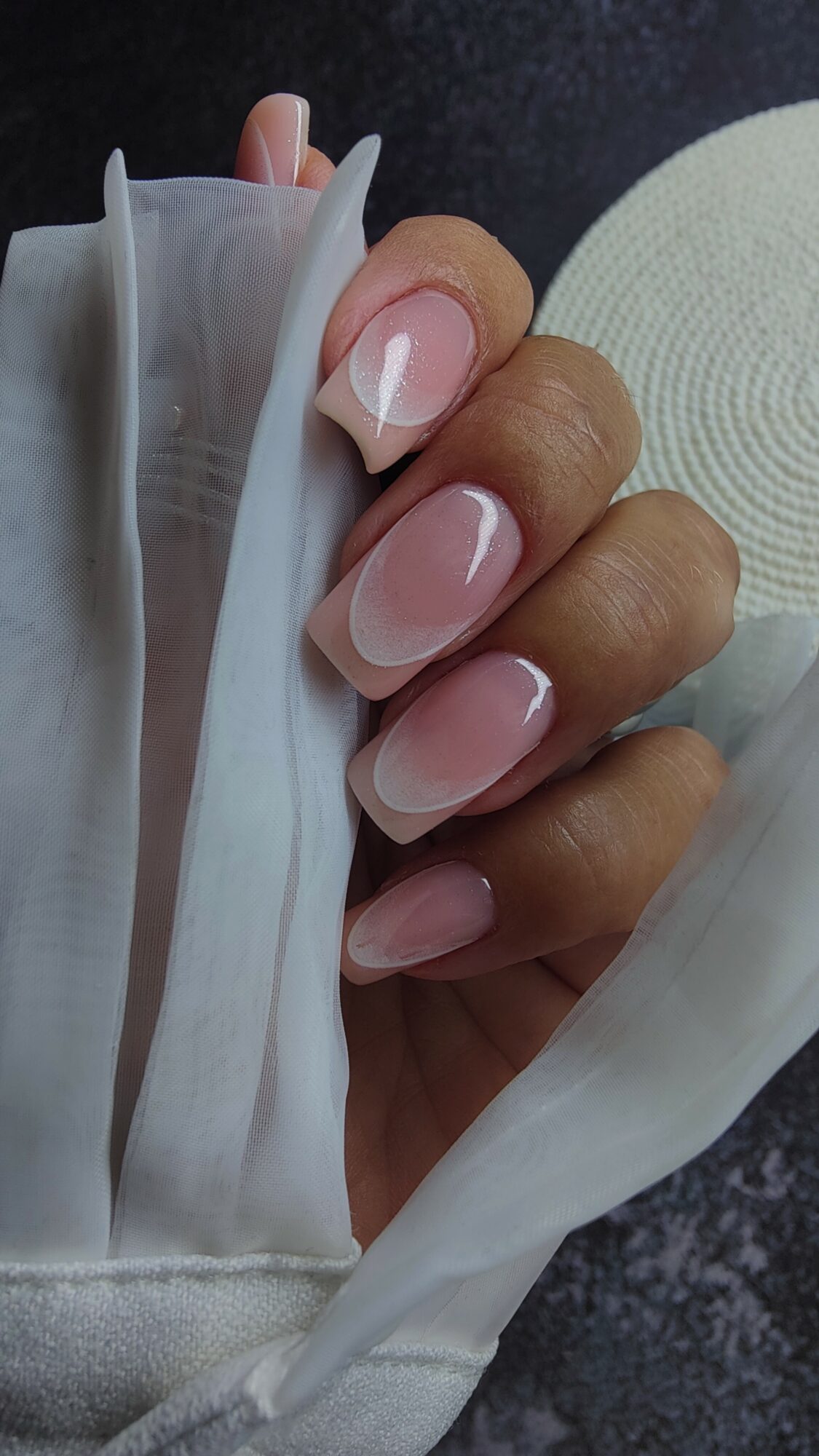 Hand with manicured nails holding a white cloth, dark background, circular textured object nearby