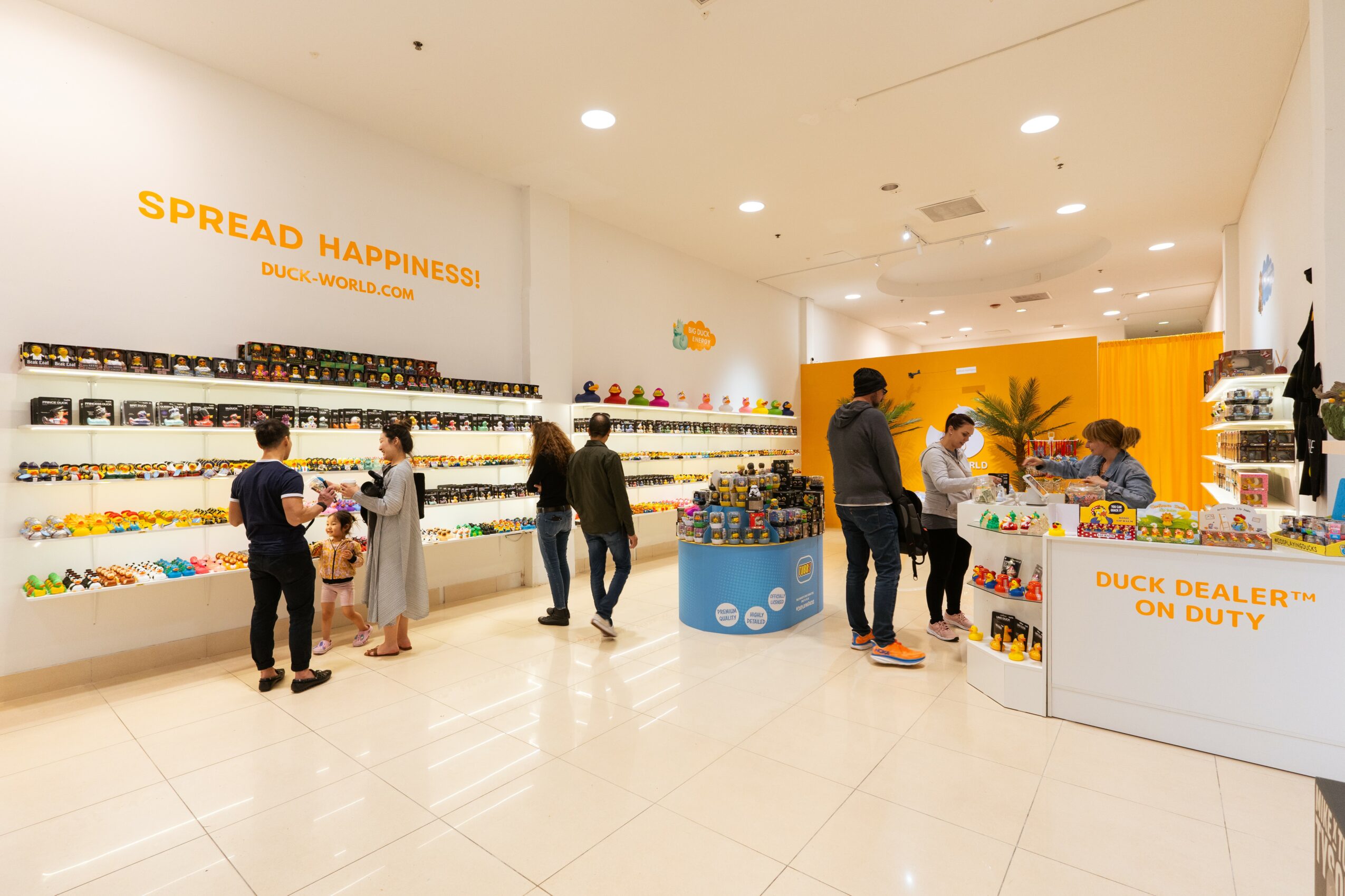 People shopping in a store with shelves of products, a counter, and a sign that reads 'Spread Happiness'.