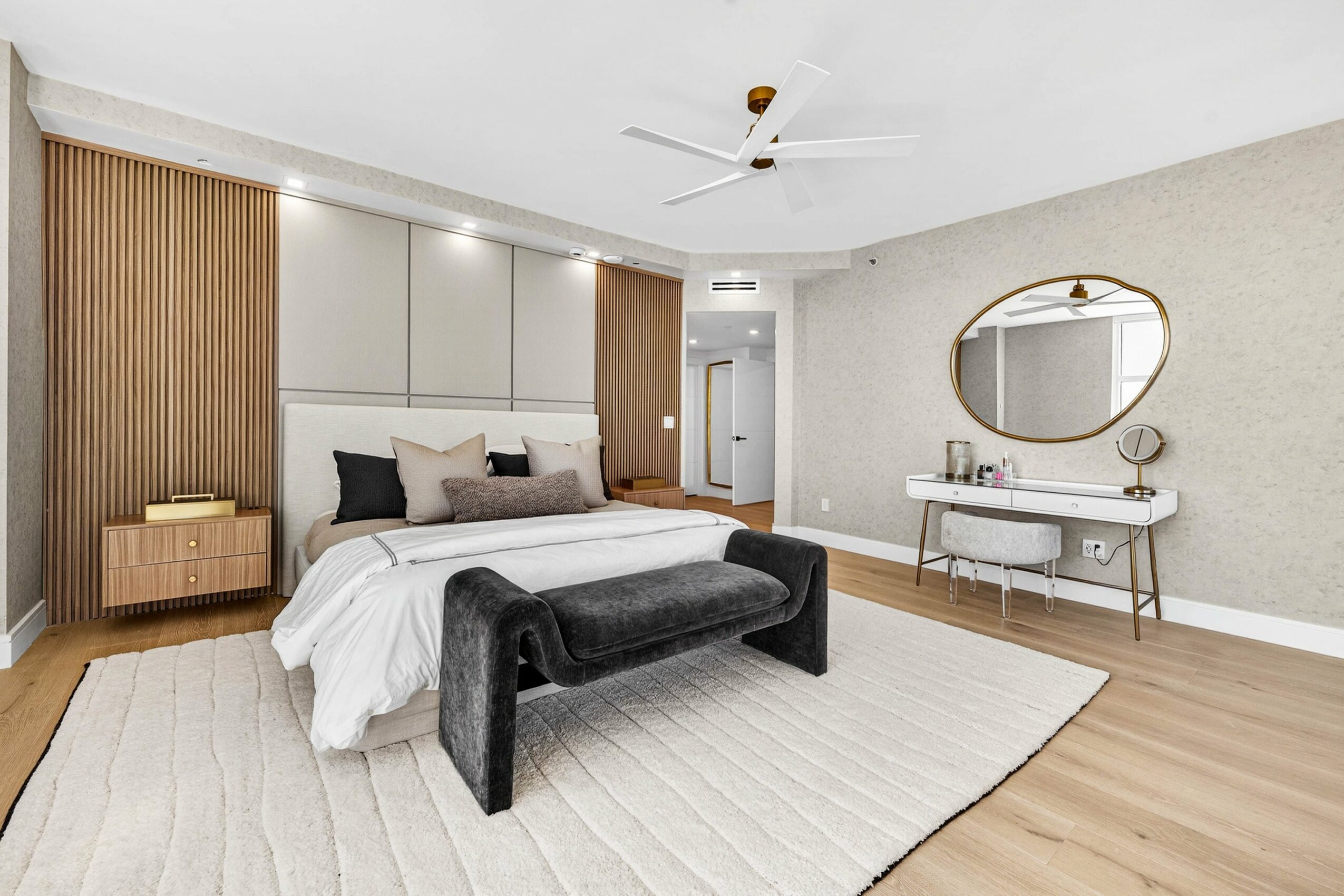 Bedroom with bed, black bench, dresser, mirror, and wooden accents, light-colored walls, and hardwood floor.