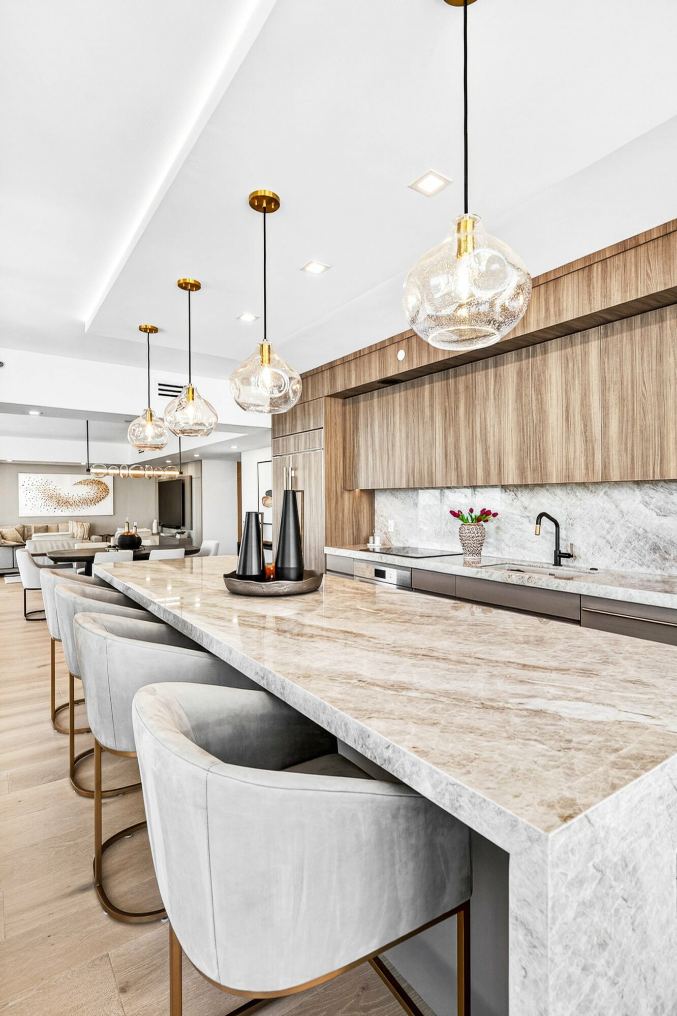 Modern kitchen with a marble island, pendant lights, and bar stools, featuring a sink and wooden cabinetry.