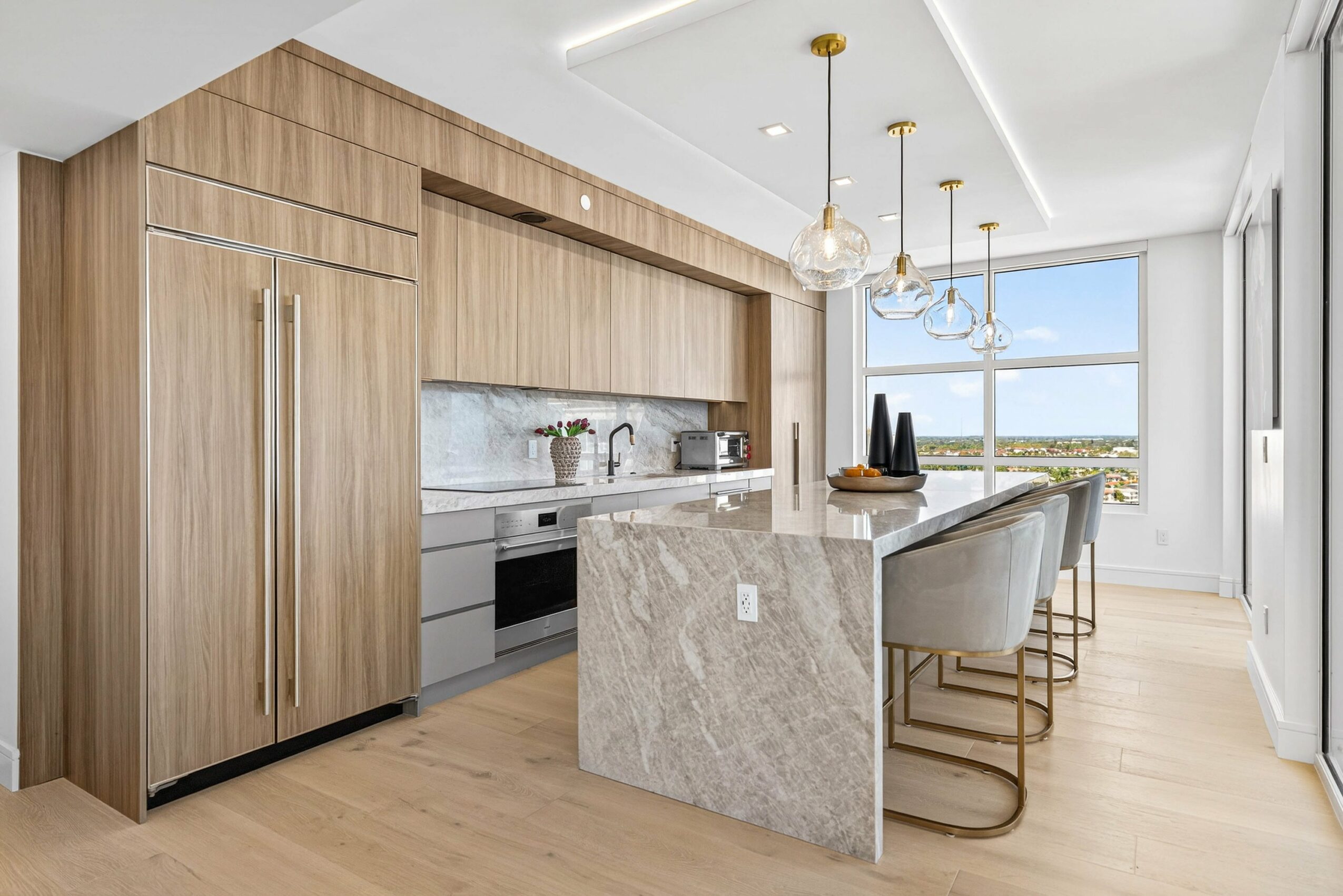 Modern kitchen with wooden cabinetry, marble island, and large window with a view, bright and airy space.