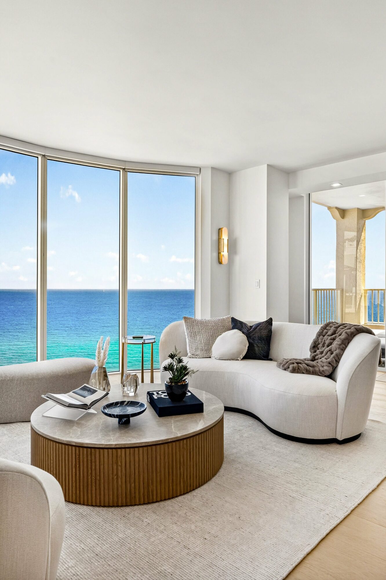 Living room with large windows showing ocean view, white sofa, round coffee table, and neutral decor.