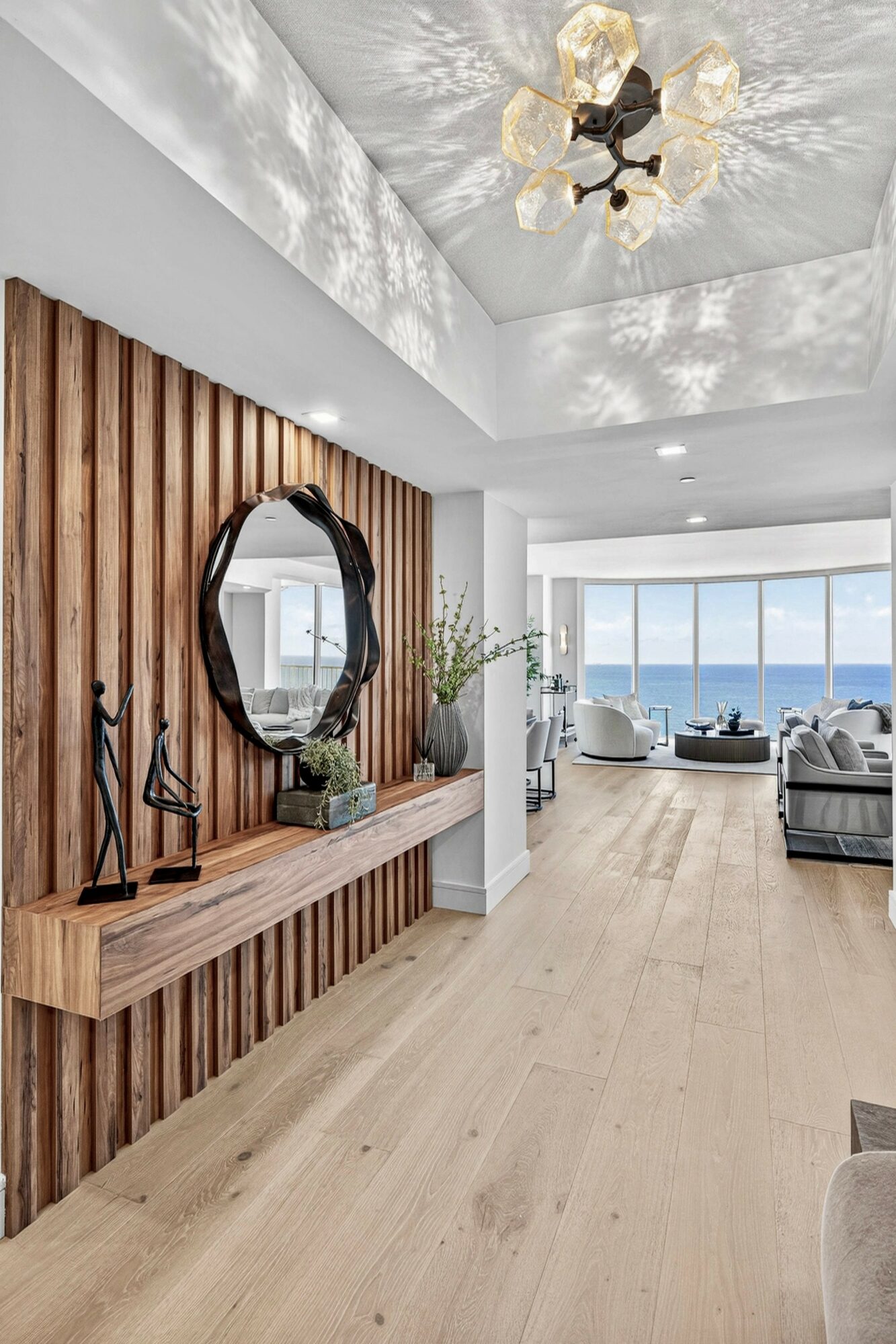 Living room with wooden wall, mirror, and large window with ocean view, bright and modern decor.