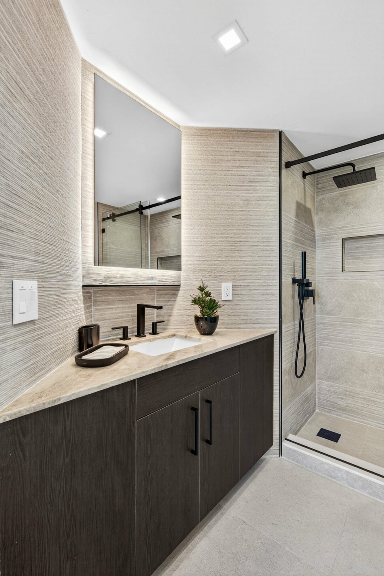 Bathroom vanity with mirror, potted plant, and soap on countertop, adjacent to a walk-in shower with black fixtures.