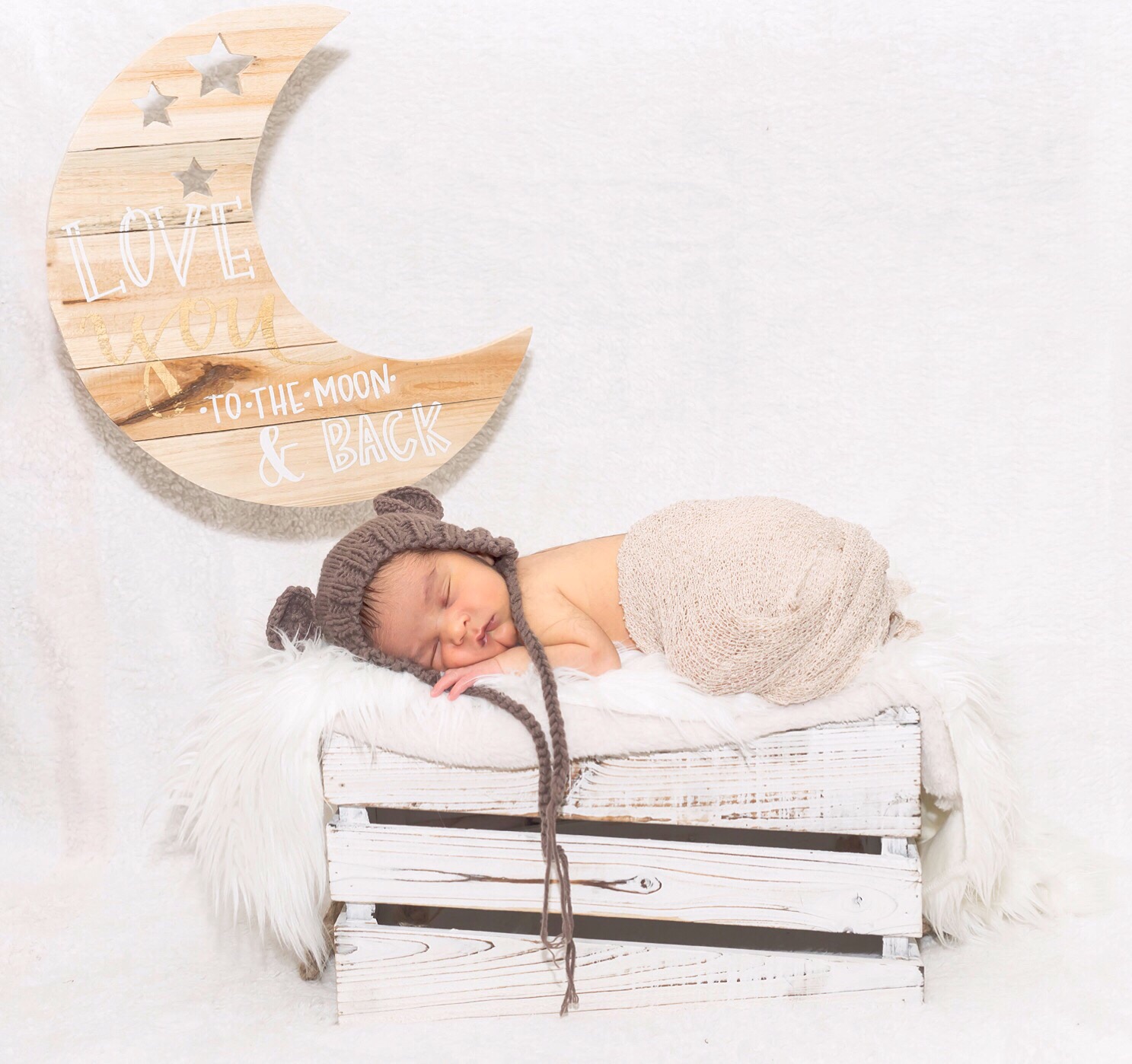 Baby sleeping on a white wooden bed with a moon-shaped wall decoration behind, in a bright, minimal setting.
