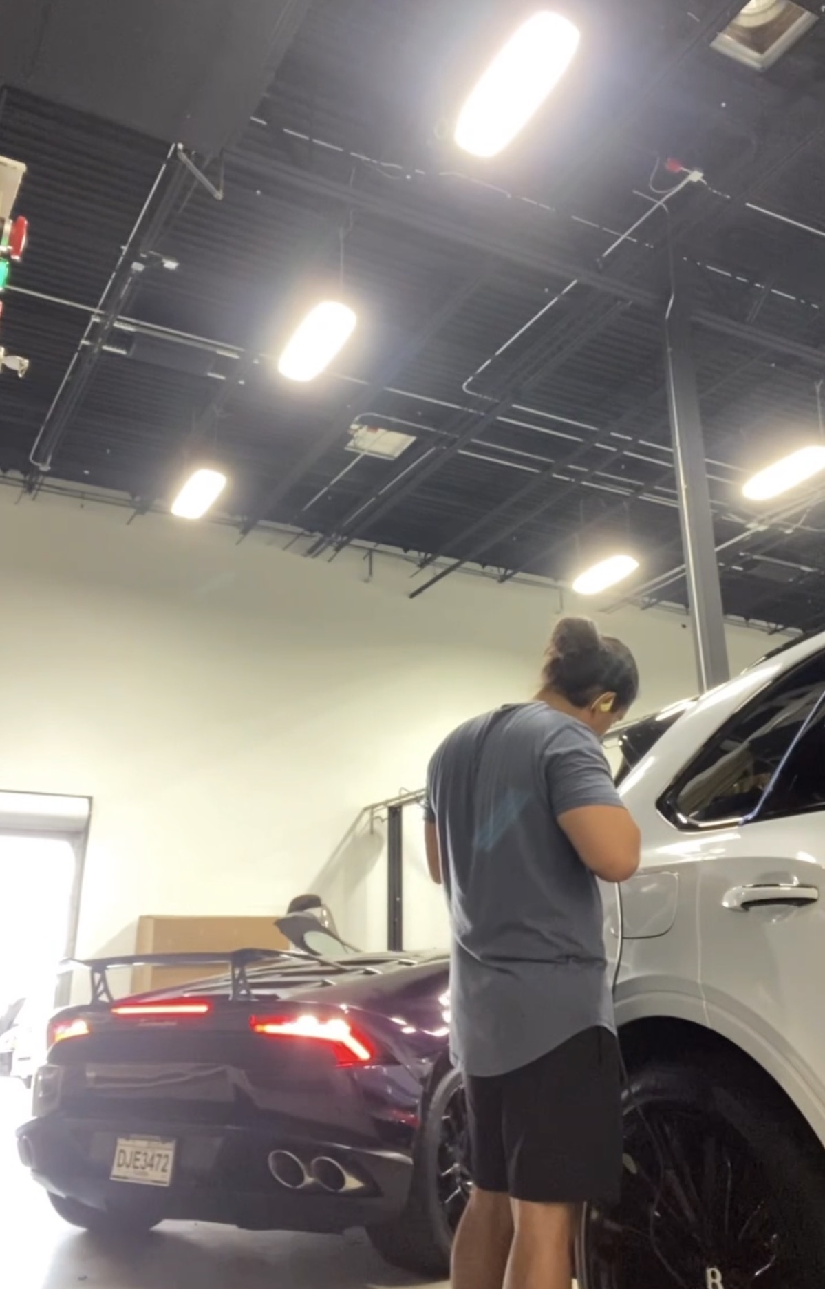 Person standing next to a white vehicle in an indoor space with bright ceiling lights.