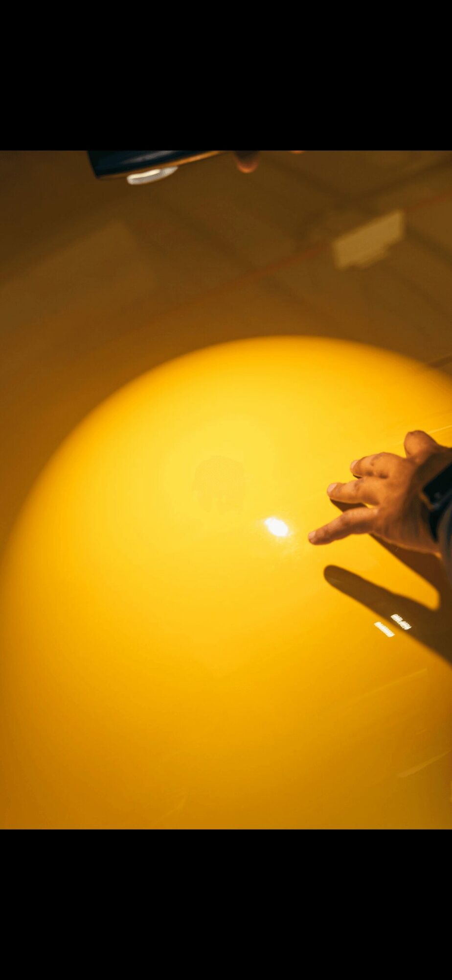 Person's hand near a bright yellow spherical object, with a shadow cast on the surface.