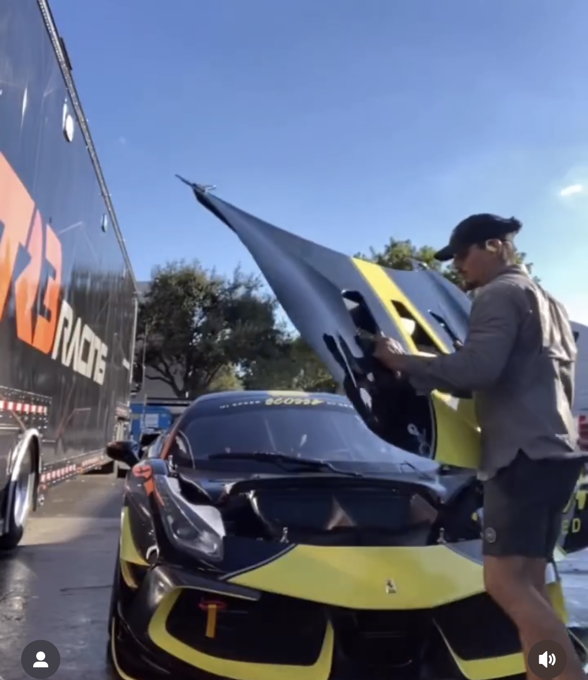 Person opening the hood of a yellow and black sports car in a parking lot, with a large truck nearby and trees in the background.