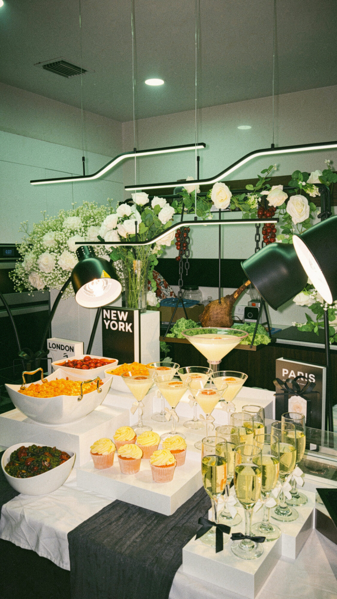 Table with bowls of snacks, drinks, and small desserts, decorated with plants and signs, in a modern indoor setting.