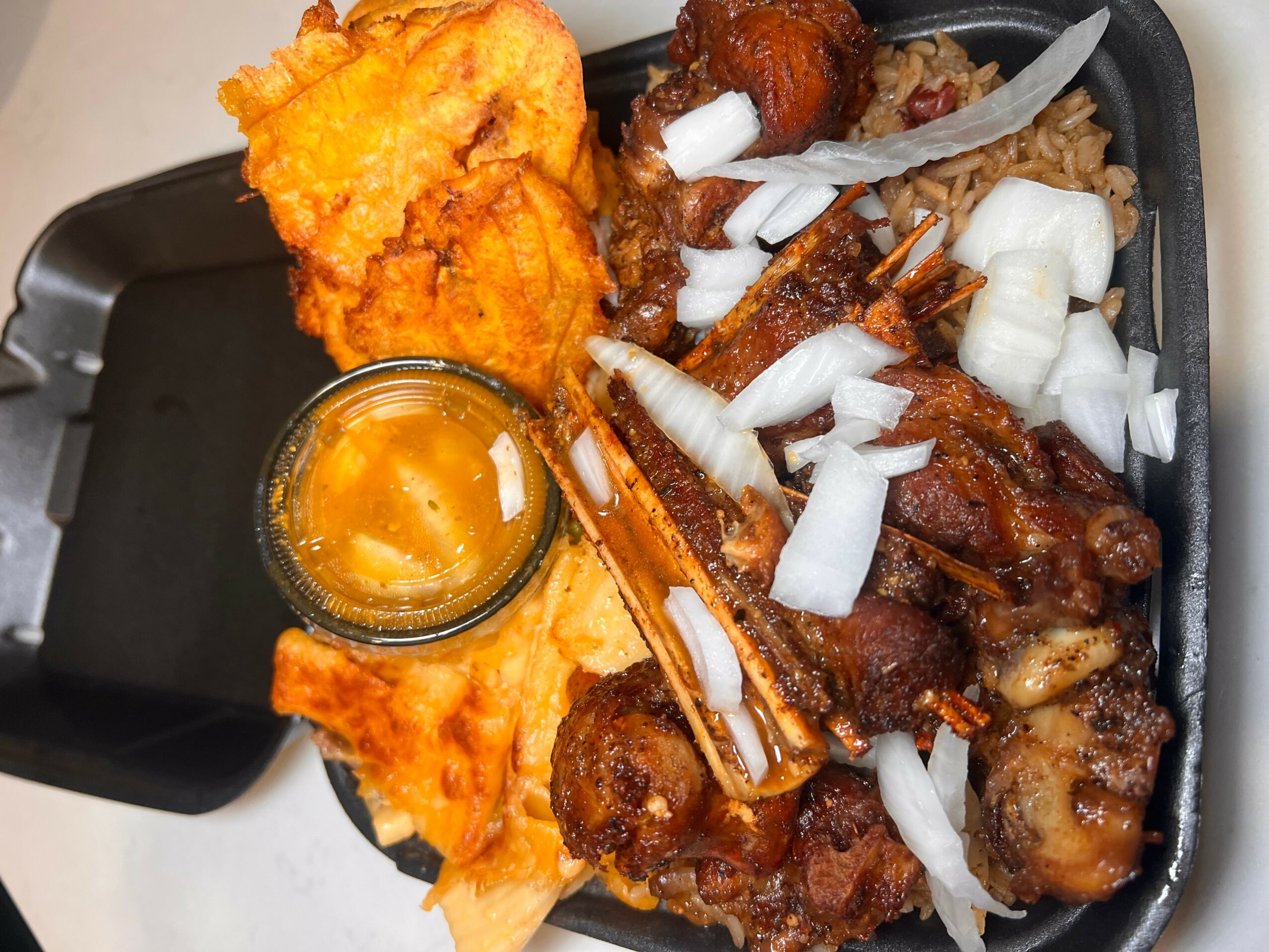 Fried chicken, onion slices, and a small container of dipping sauce on a black tray.