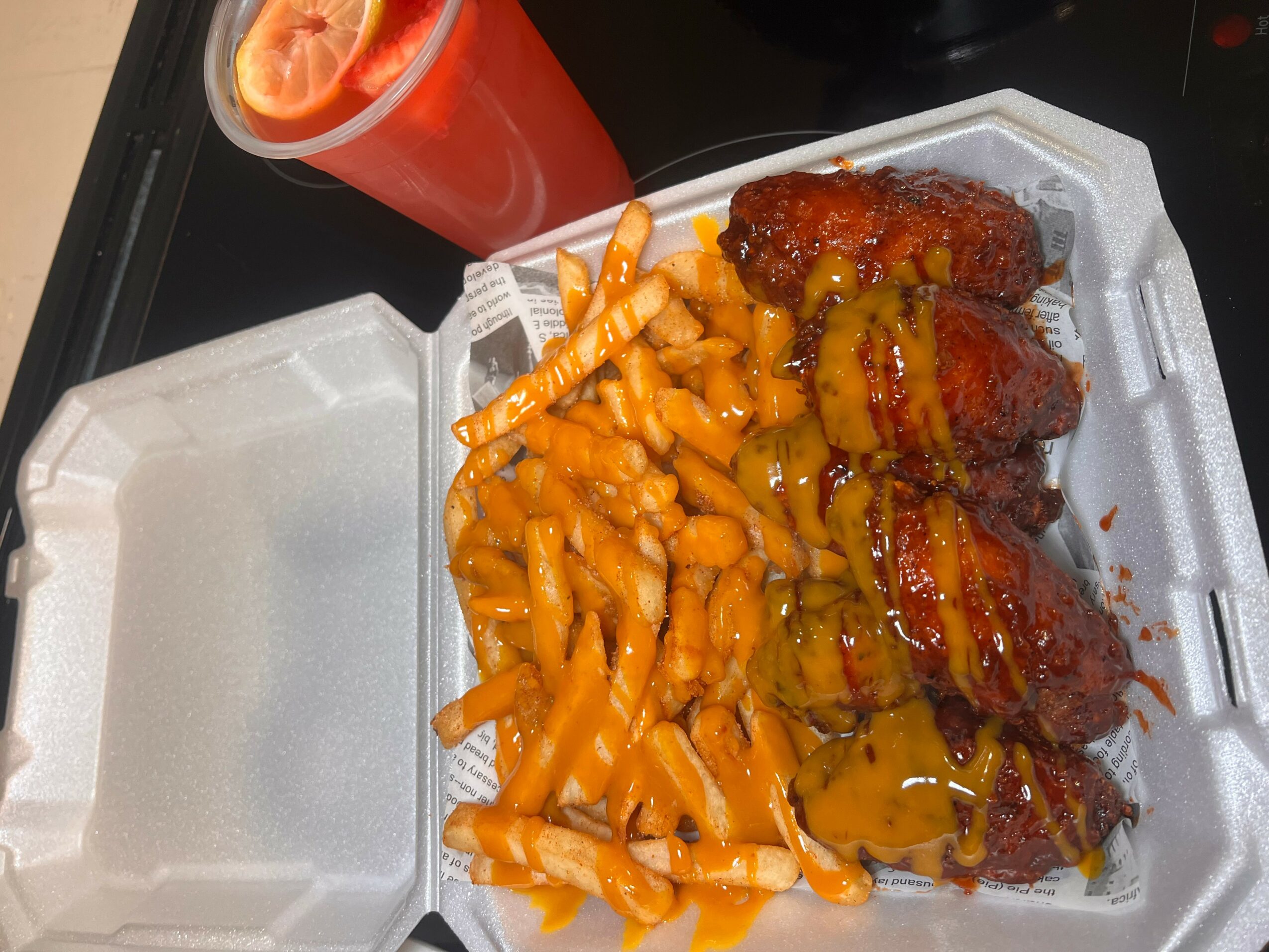 Takeout container with fried chicken, fries, and a drink in a red cup, on a black surface.