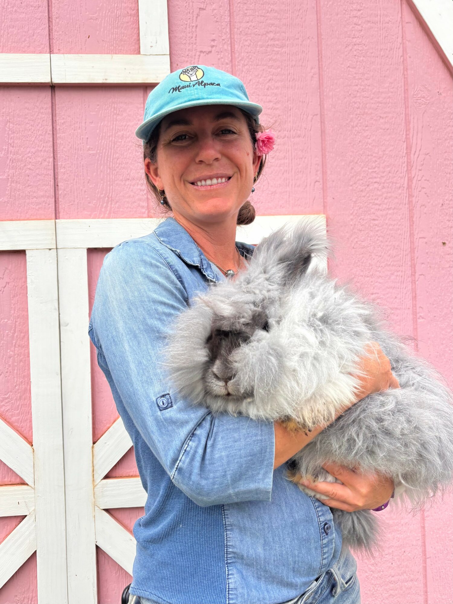 Smiling woman holding a fluffy rabbit in front of a pink and white wooden fence.