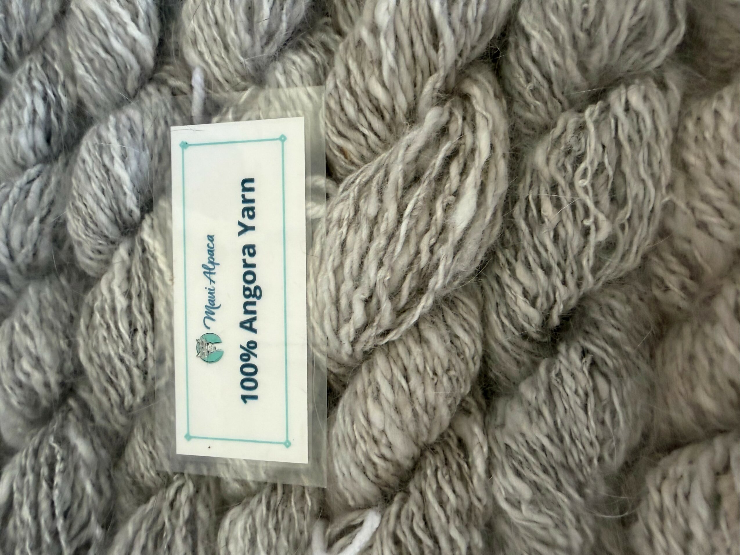 Close-up of beige and gray yarn skeins with a label reading '100% Angora Yarn'.