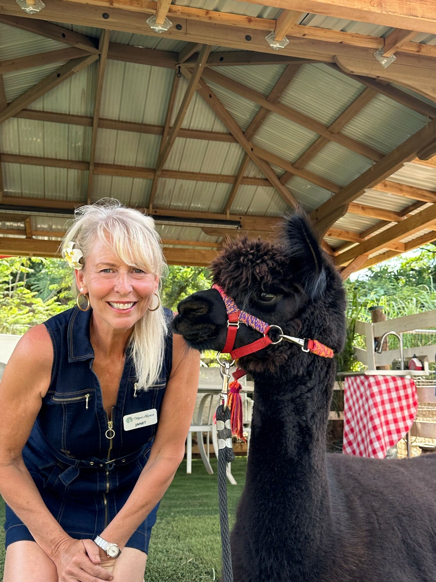 Woman with blonde hair and glasses smiling next to a black horse in a wooden shelter.
