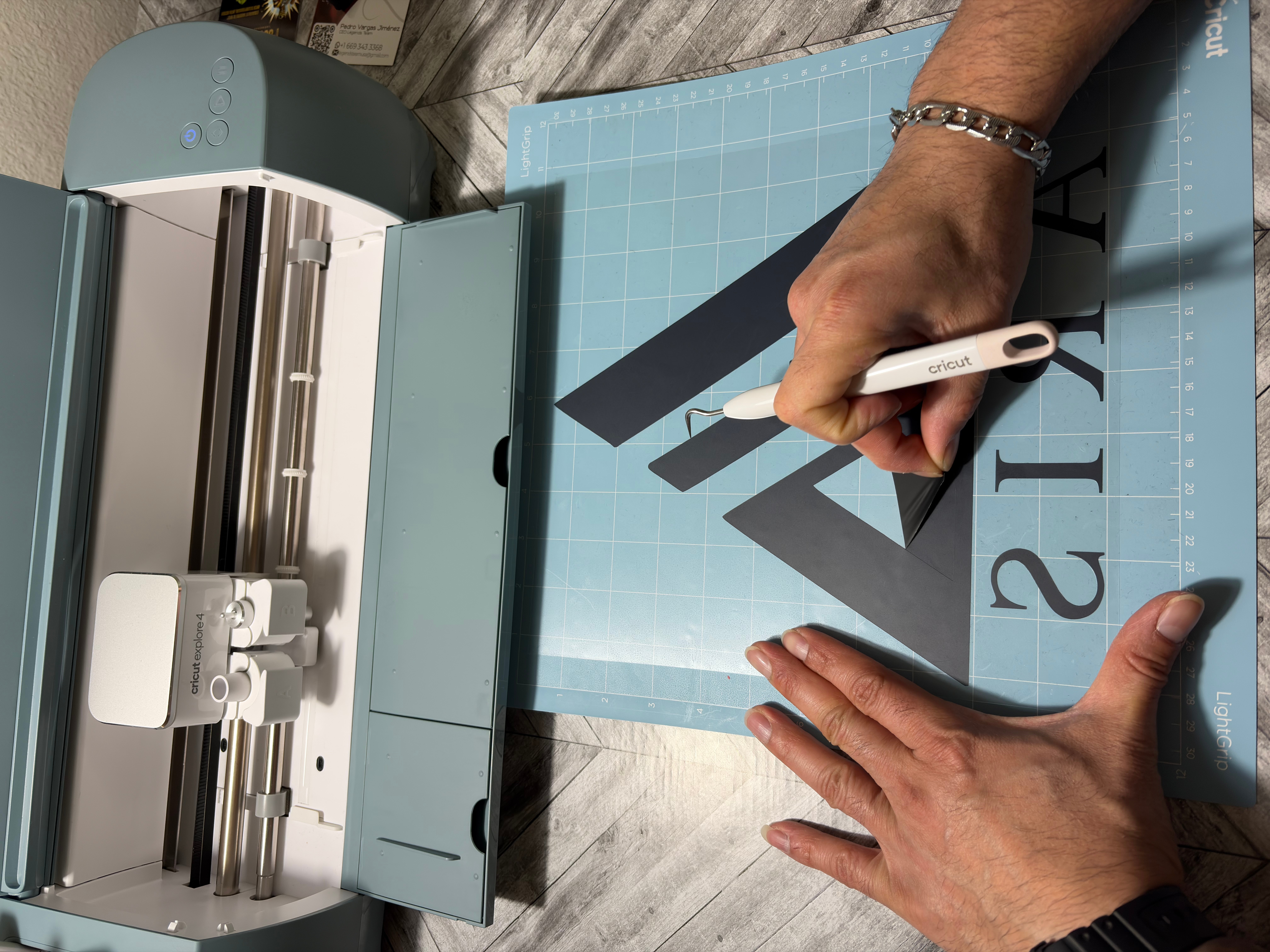 Person using a cutting machine to cut a black letter on a blue grid cutting mat, with hands visible.