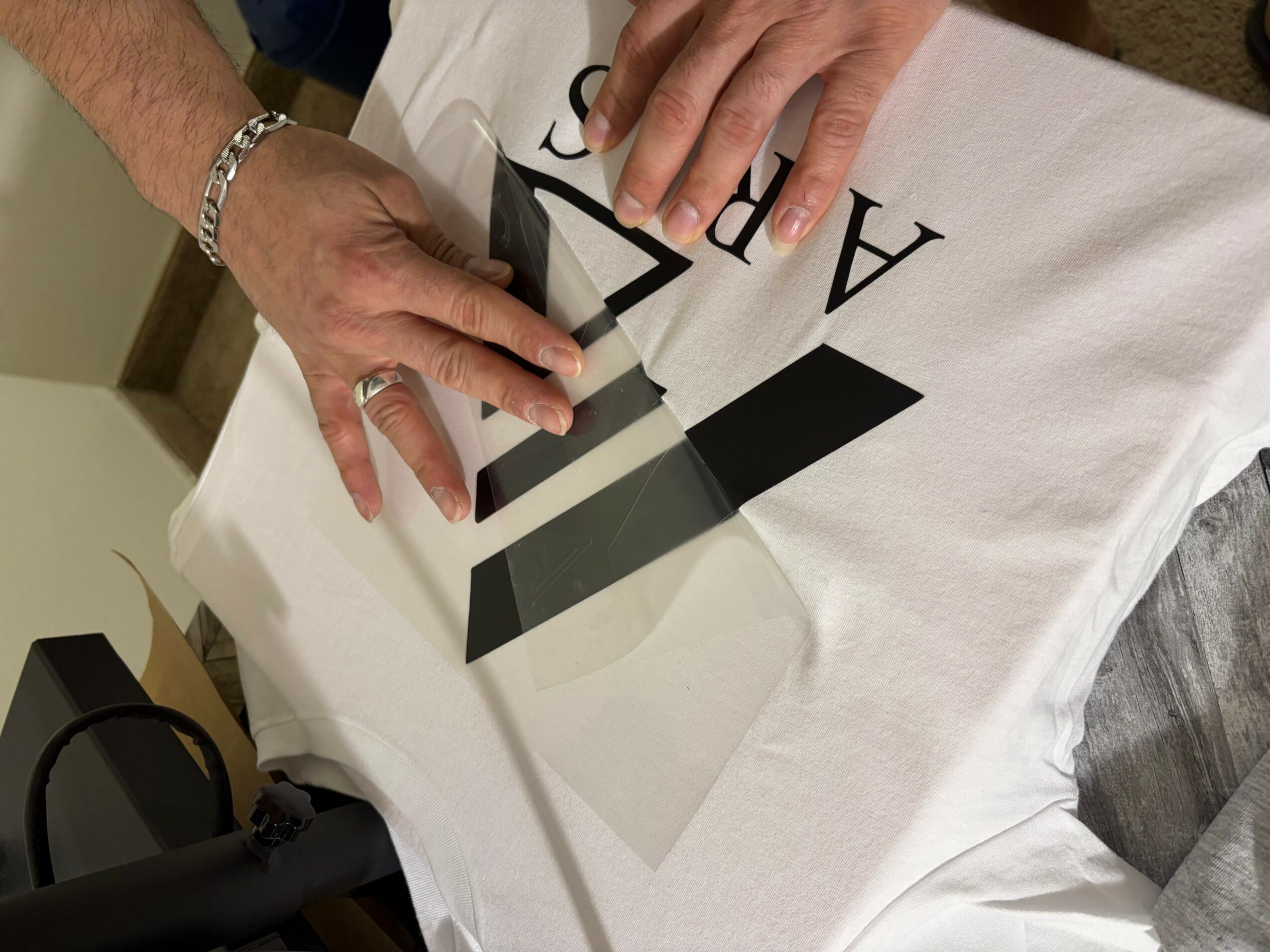 Hands with rings and bracelet place a black and gray geometric object on a white cloth with text.
