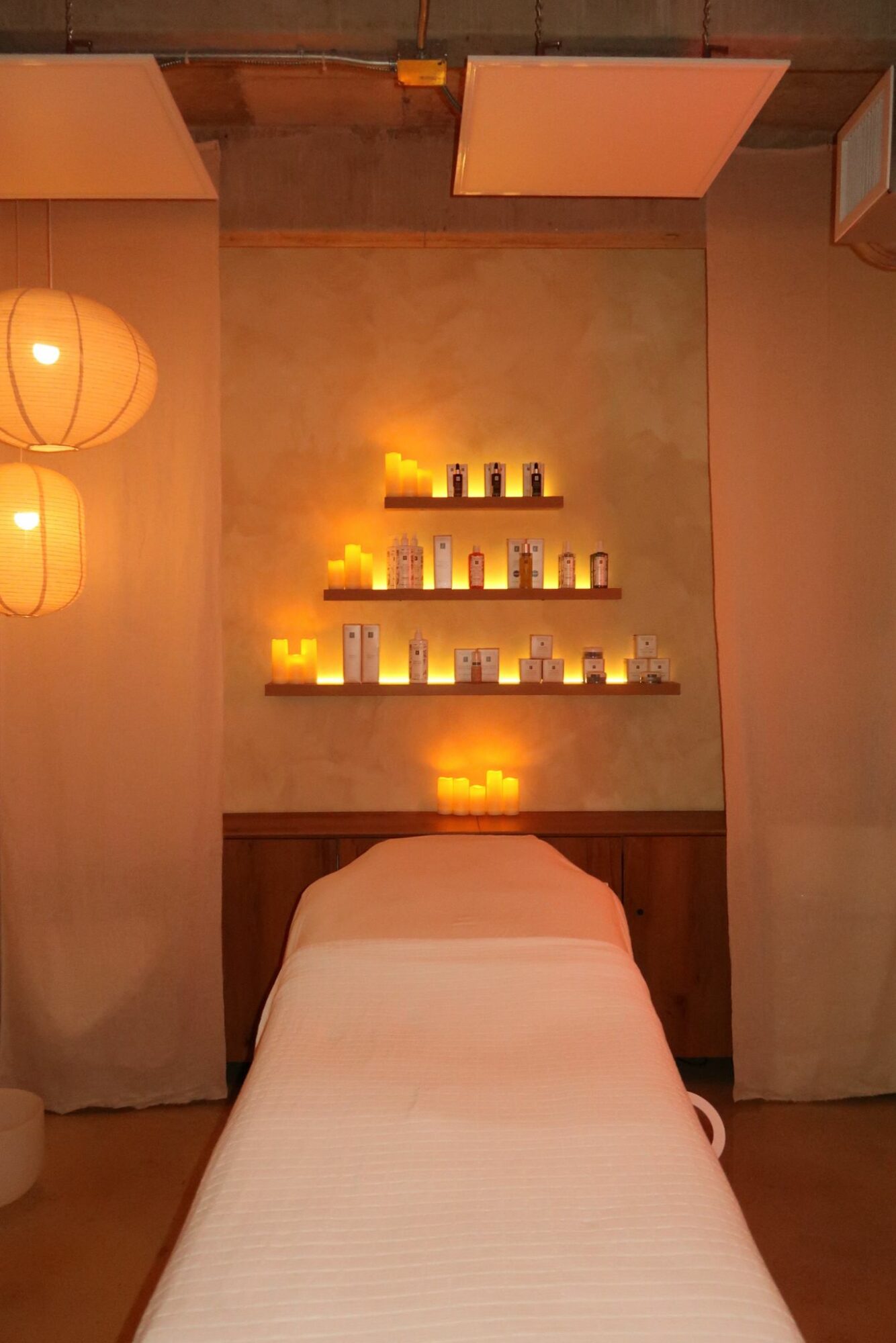 Massage table in a softly lit room with candles and shelves on the wall, warm ambient lighting, and paper lanterns.