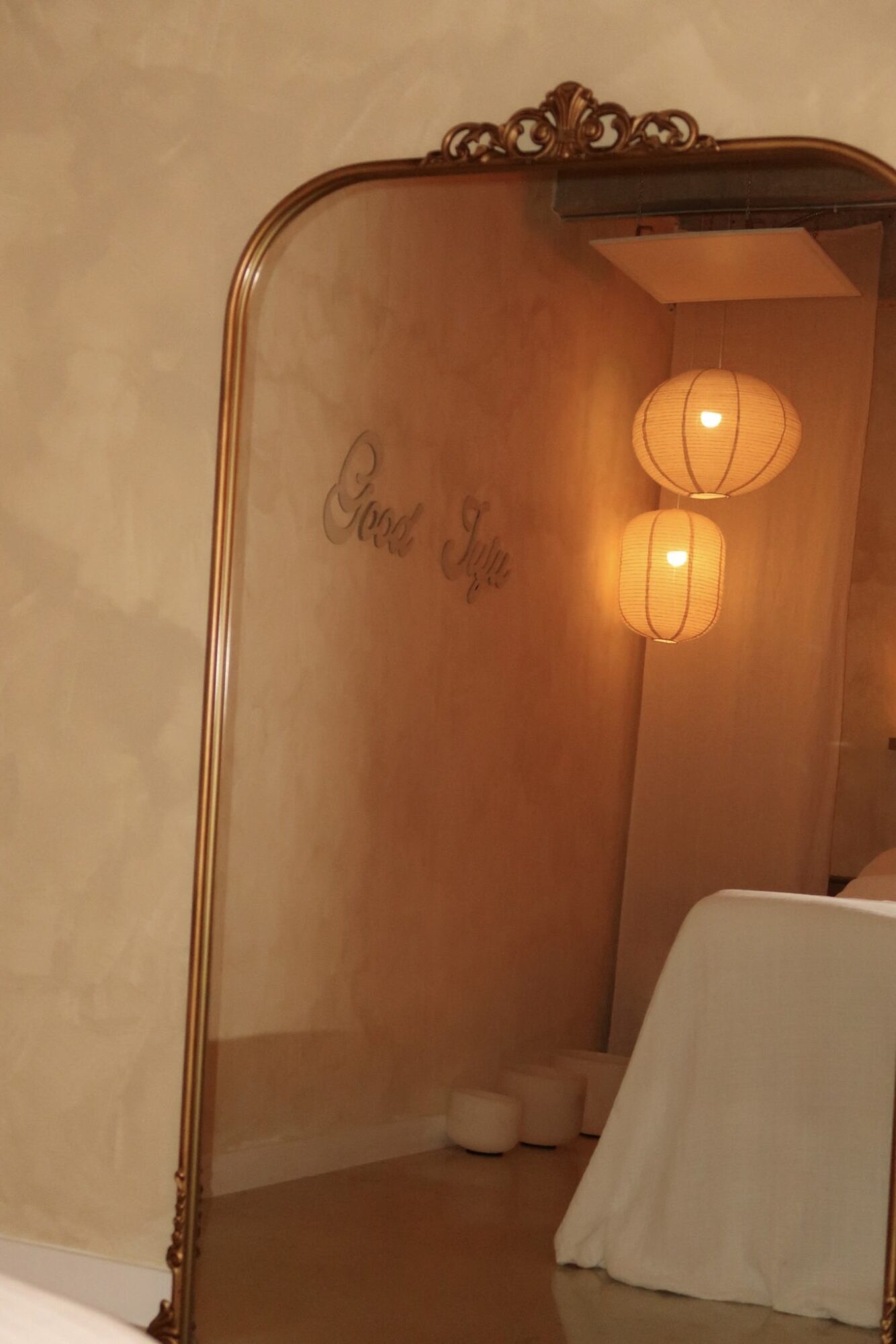 Decorative mirror with a gold frame reflecting a wall with hanging paper lanterns and a table covered with a white cloth.