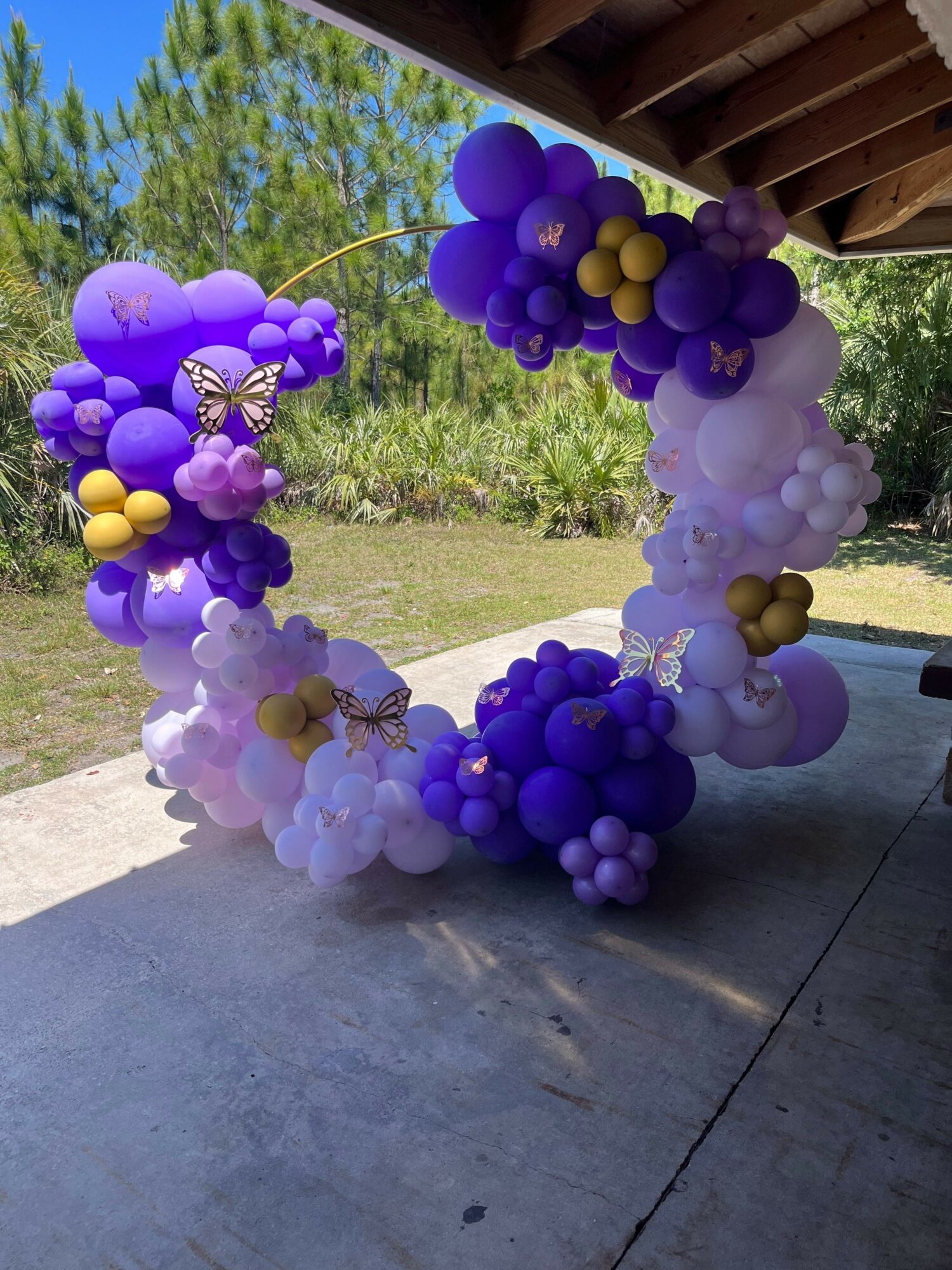 Colorful balloon arch with purple, pink, white, and gold balloons outdoors, decorated with butterfly and star shapes.
