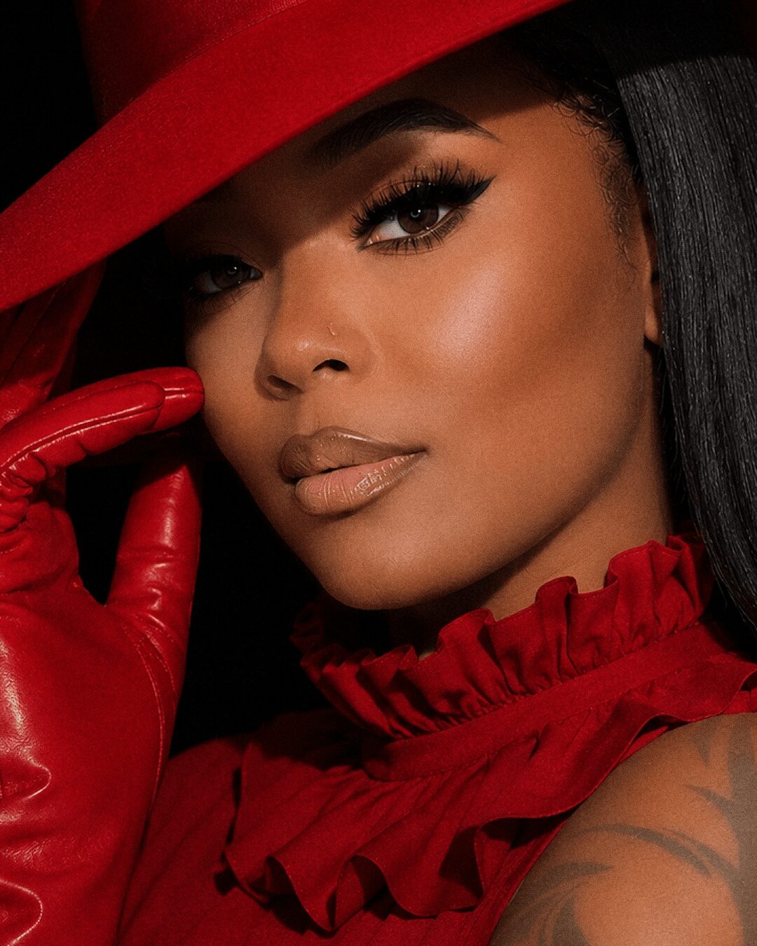 Woman with makeup, red hat, red ruffled top, and red glove touching her face.