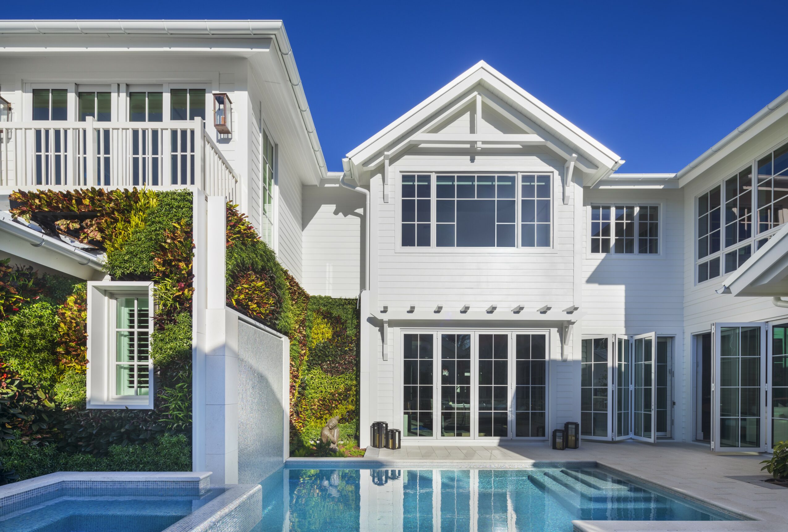 Modern white house with large windows and a swimming pool in the backyard, under a clear blue sky.