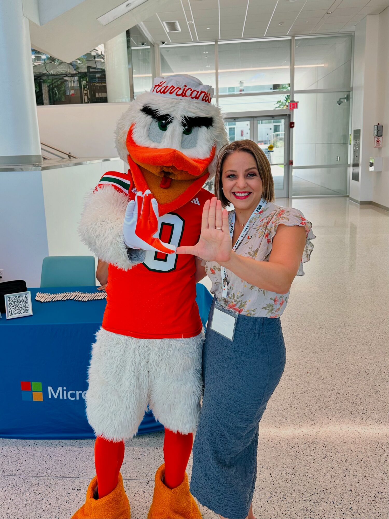 Woman smiling with a person in a bird mascot costume in a bright indoor space.