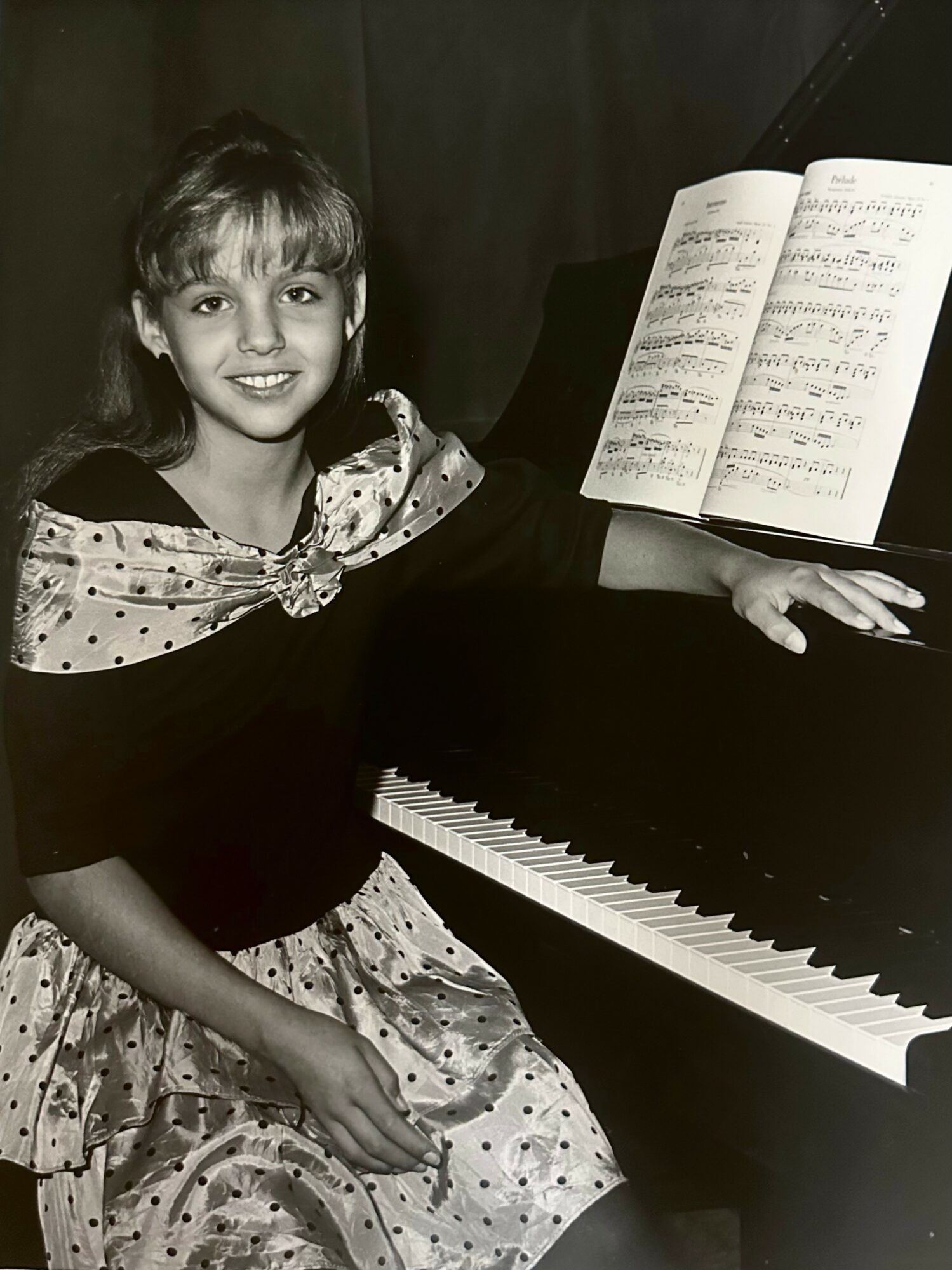 Young girl sitting at a piano with sheet music open, smiling at the camera.