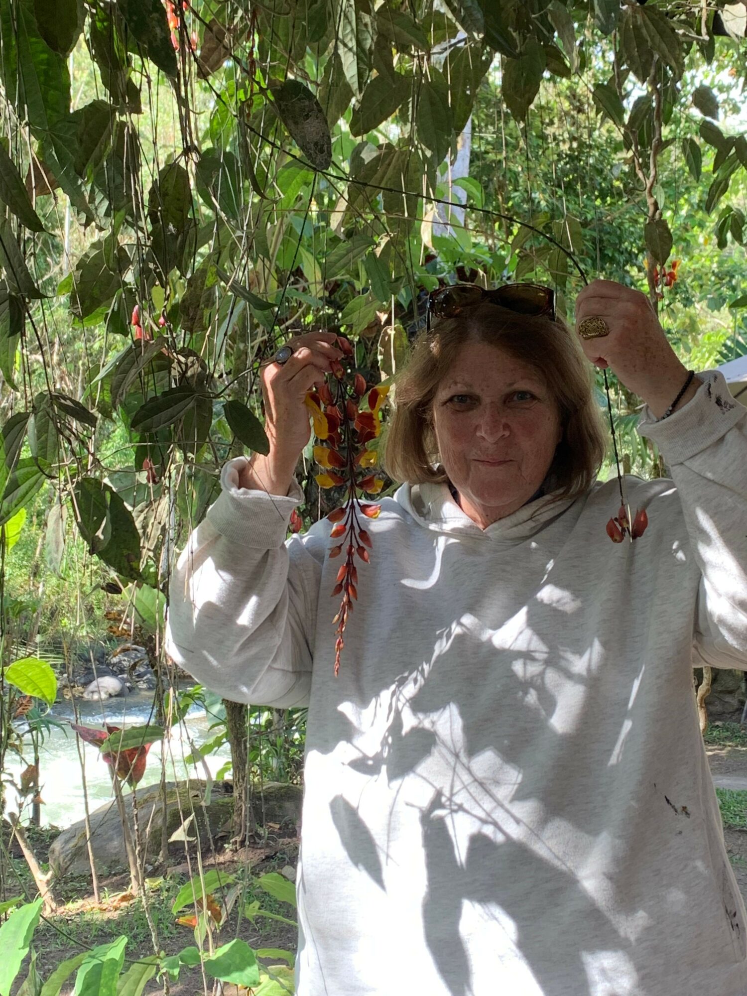 Woman in white dress holding a colorful bouquet, standing among green plants outdoors.