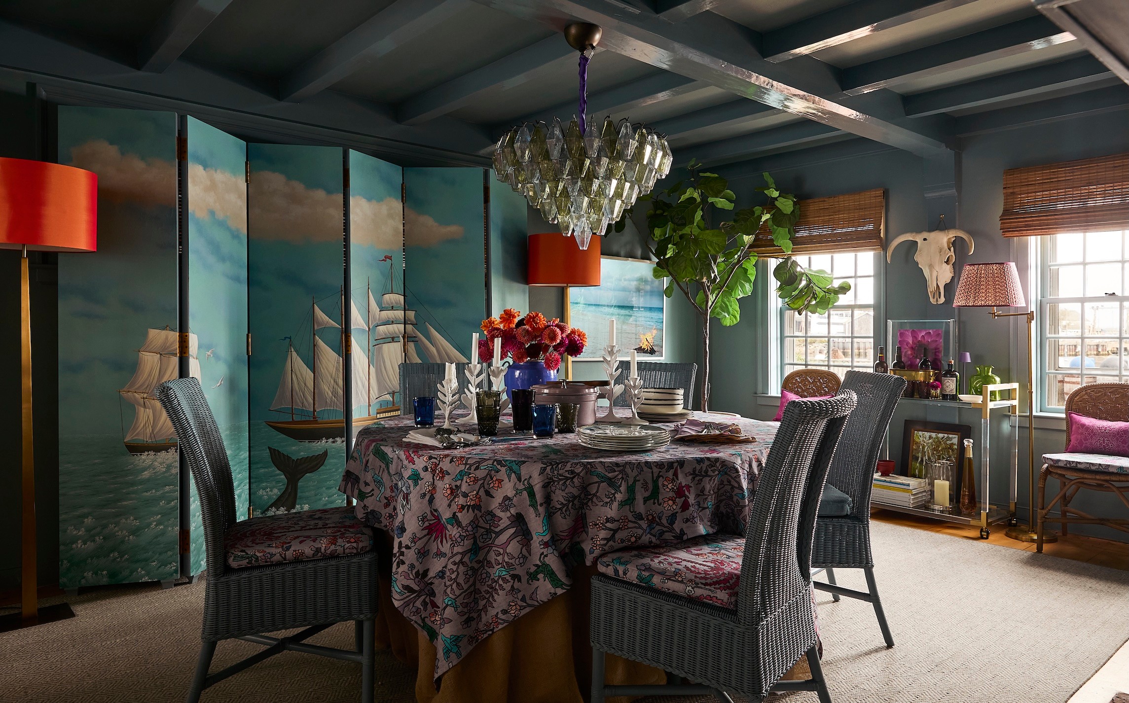 Dining room with a round table, four chairs, a chandelier, and a painted ocean scene on the wall.