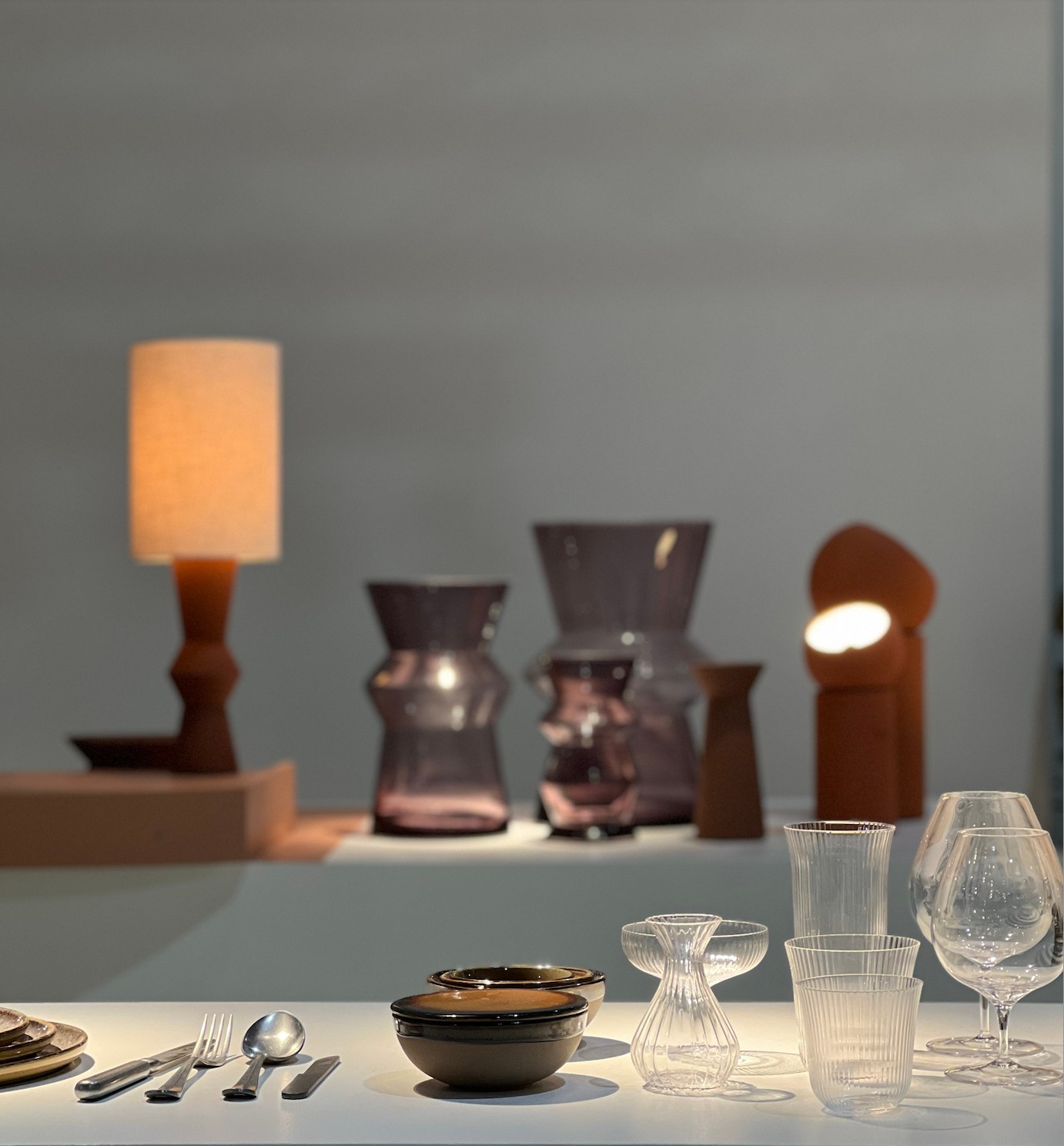 Table setting with bowls, glasses, and cutlery, with decorative lamps in the background.