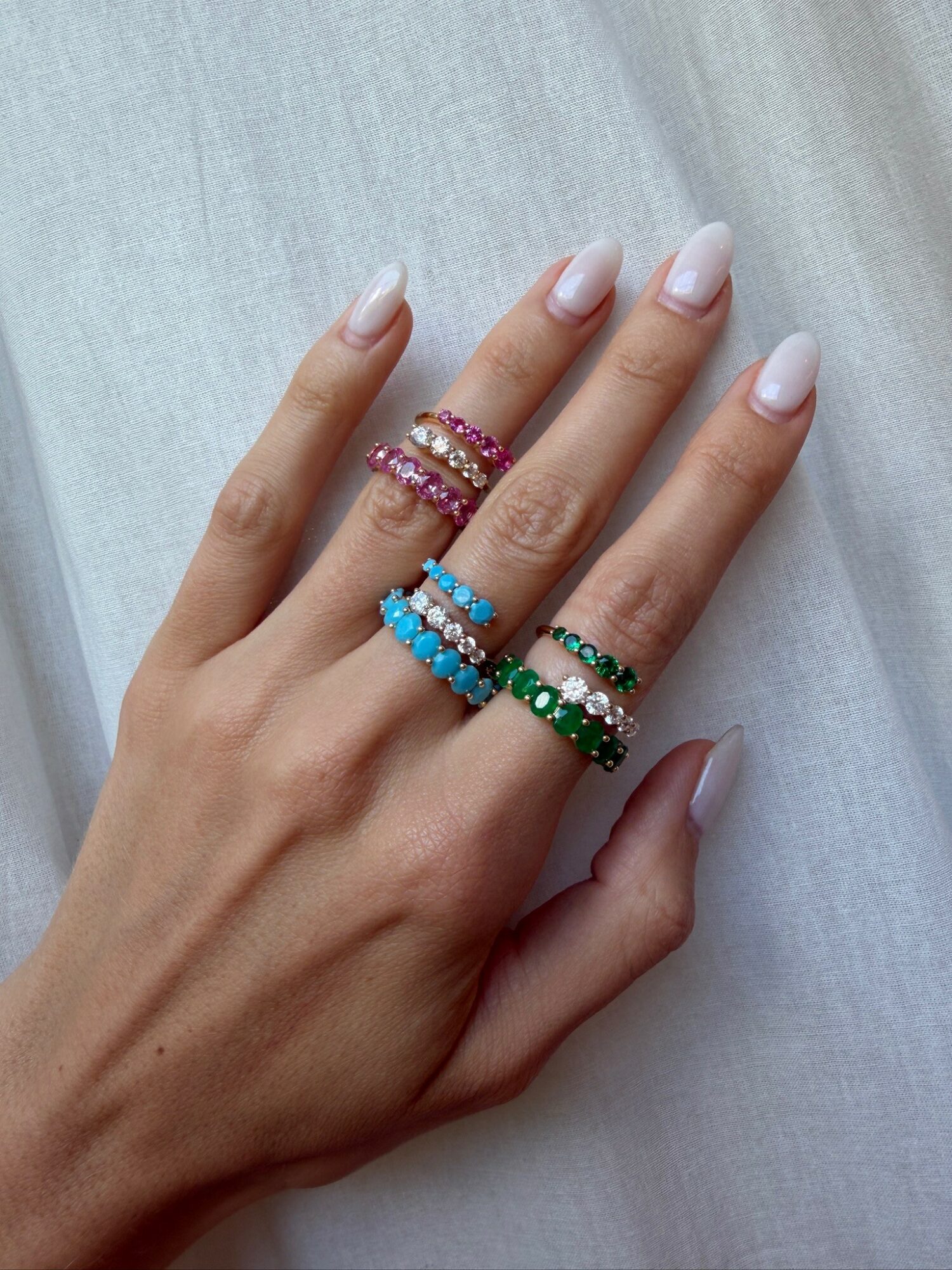 Hand with five rings featuring pink, blue, green, and black beads, resting on light fabric.
