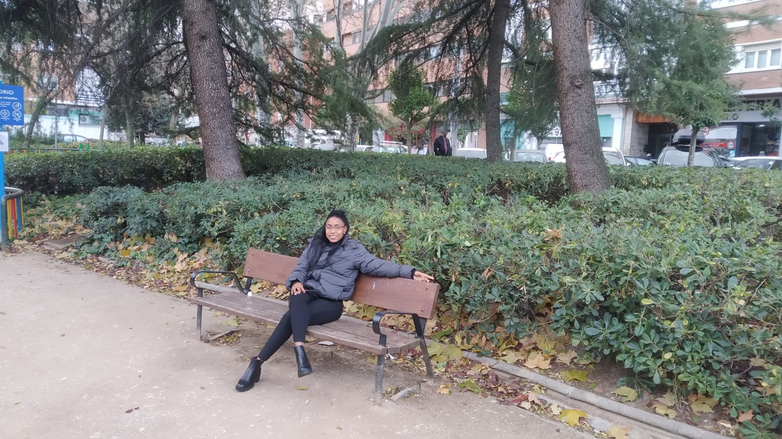 Person sitting on a park bench with trees and bushes in the background.