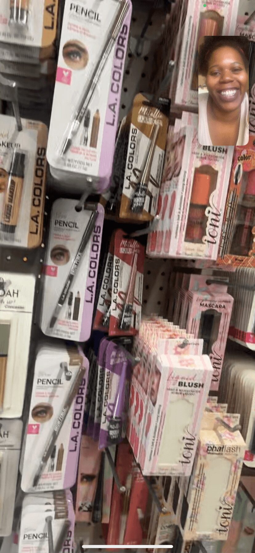 Display of various makeup and cosmetic products, including pencils and lip glosses, with a smiling woman in the background.