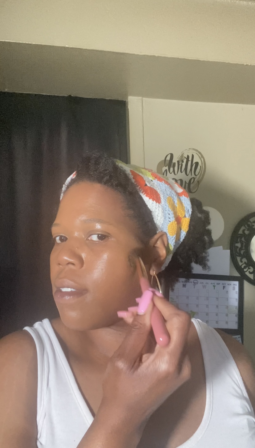 Person with colorful headscarf applying makeup or skincare, wearing a white sleeveless top, indoors.