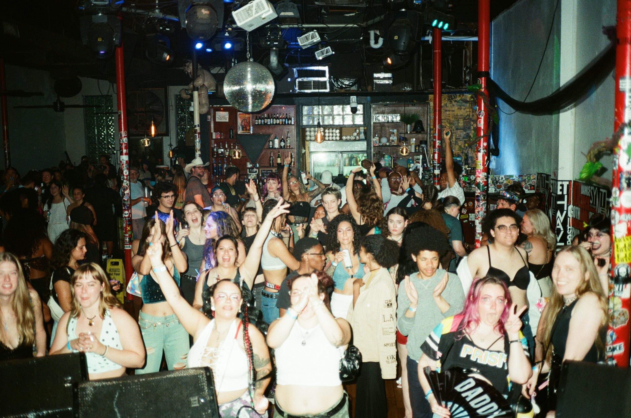 Crowd of people dancing and enjoying a party in a nightclub with colorful lights and decorations.