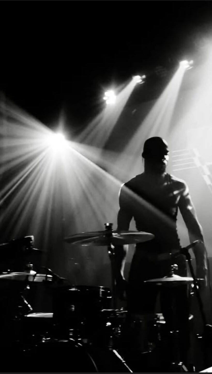 Silhouette of a person on stage with bright lights shining behind, musical instruments visible, black and white image.