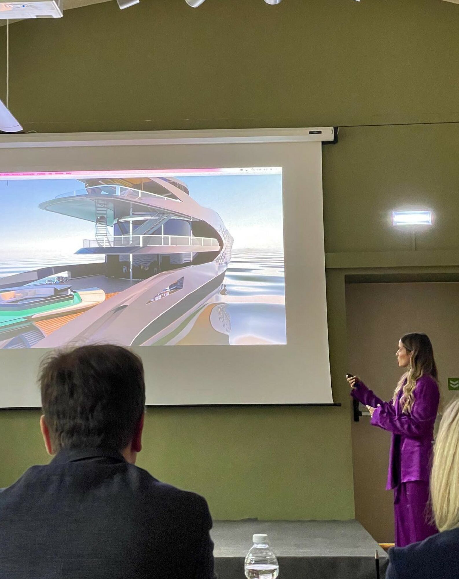 Woman in purple outfit presenting a futuristic train model on a screen in a classroom setting.