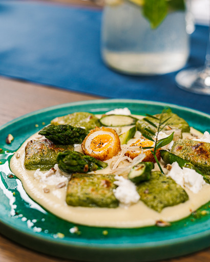 Plate with grilled zucchini, cucumber slices, and herbs on a green dish, with a blurred background of a glass and a jar.
