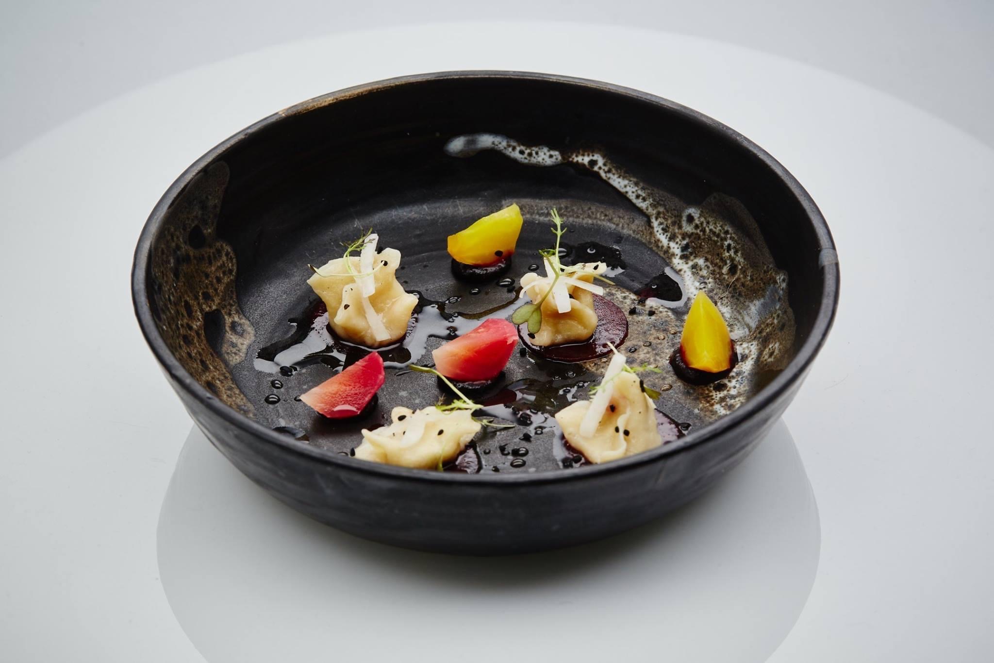 Empty black bowl with small food pieces and colorful garnishes inside, on a white surface.