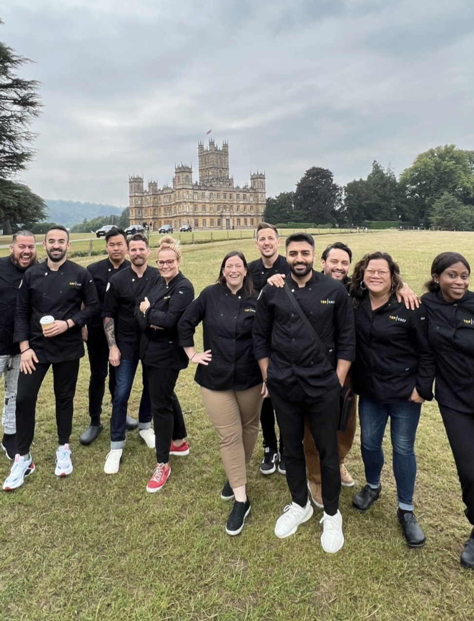 Group of people standing outdoors on grass with a castle in the background, smiling and posing for a photo.