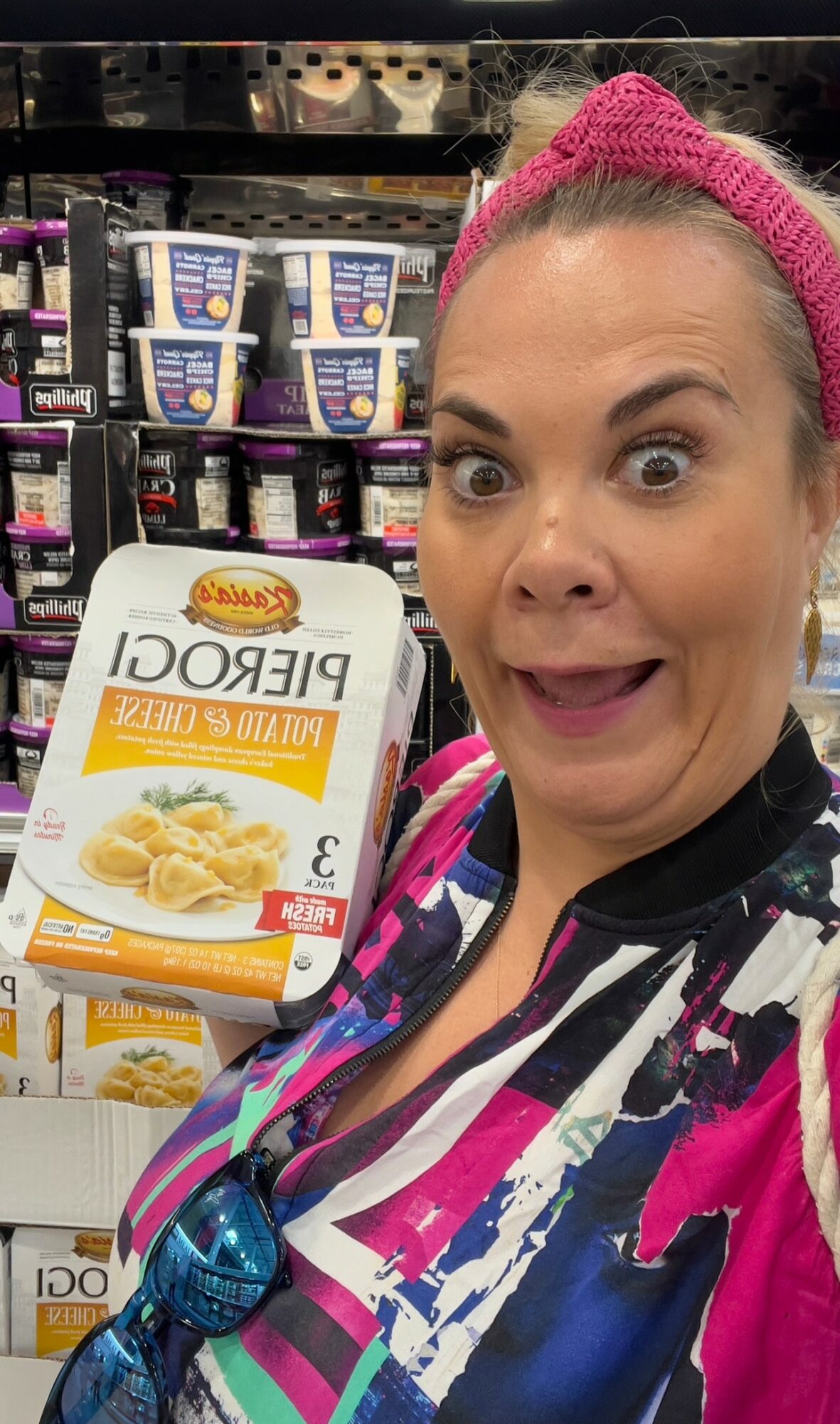 Woman with pink headband holding a box of frozen pasta, shelves of food products in background.
