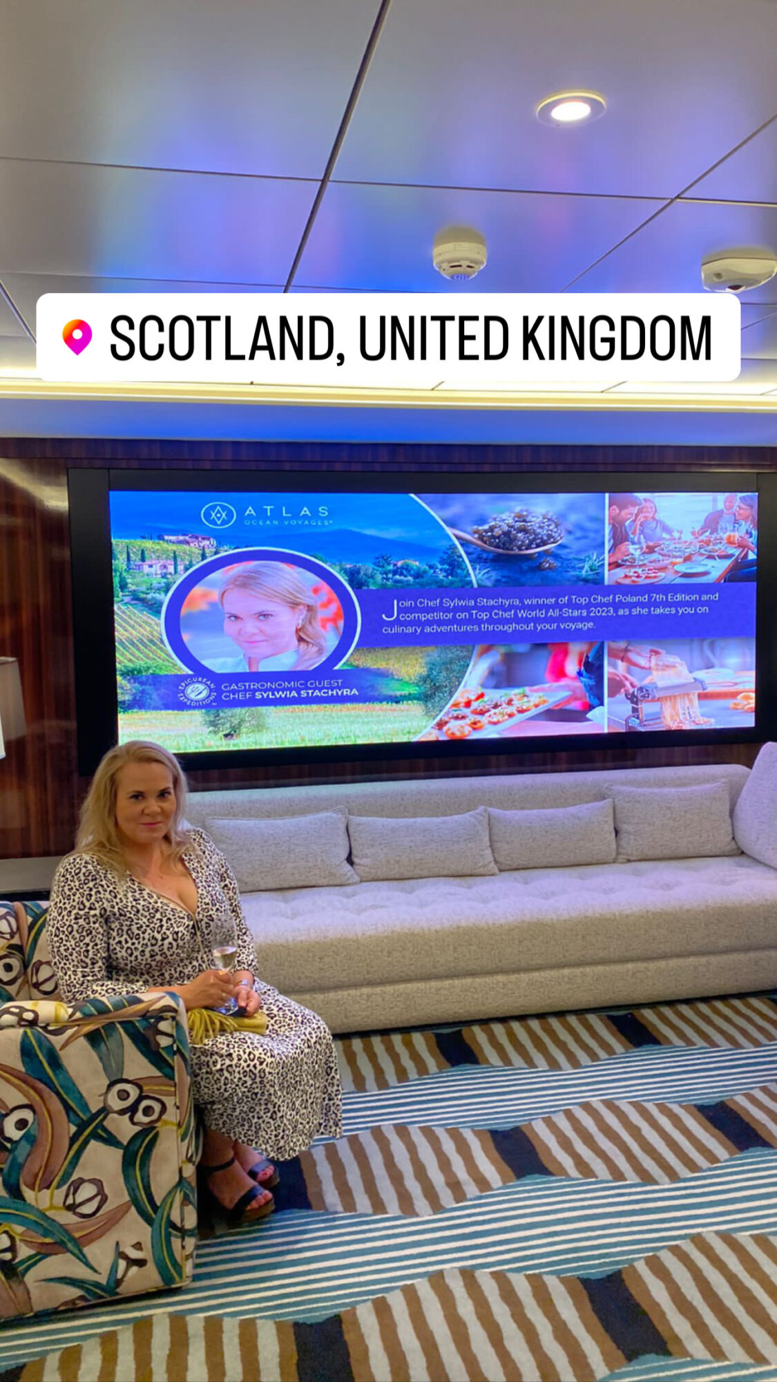 Woman sitting on a sofa in a waiting area with a large screen behind her displaying travel information, in Scotland, United Kingdom.