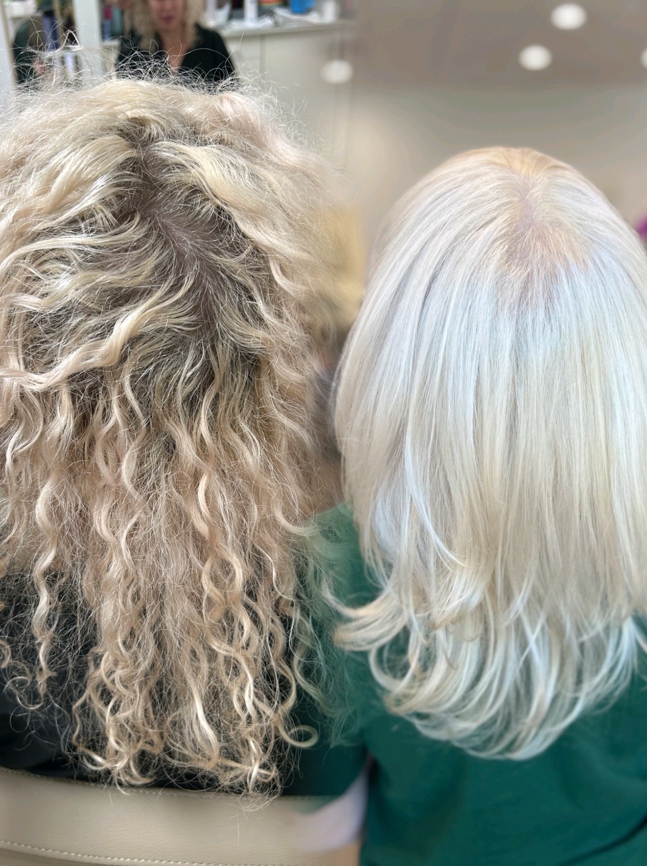 Two people with curly and straight hair, viewed from behind, in a well-lit indoor setting.