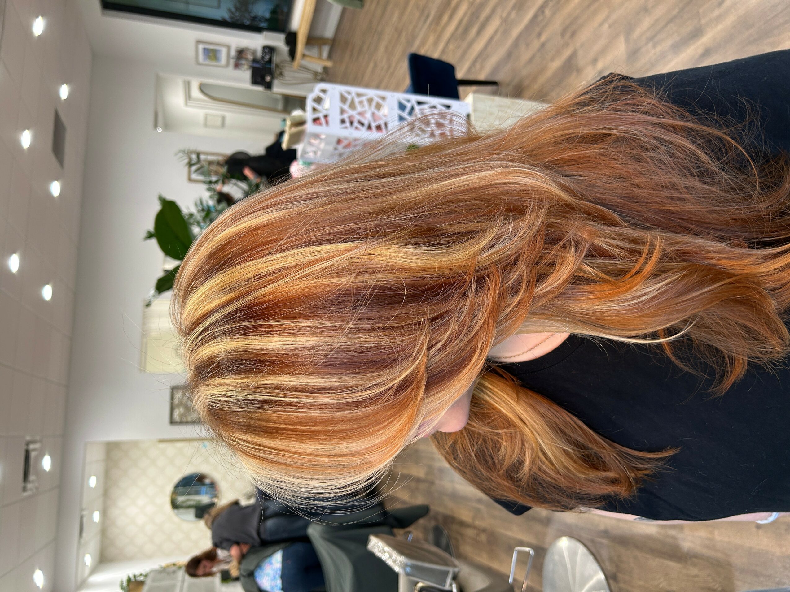 Side view of a woman with long, wavy, reddish-blonde hair in an indoor setting.