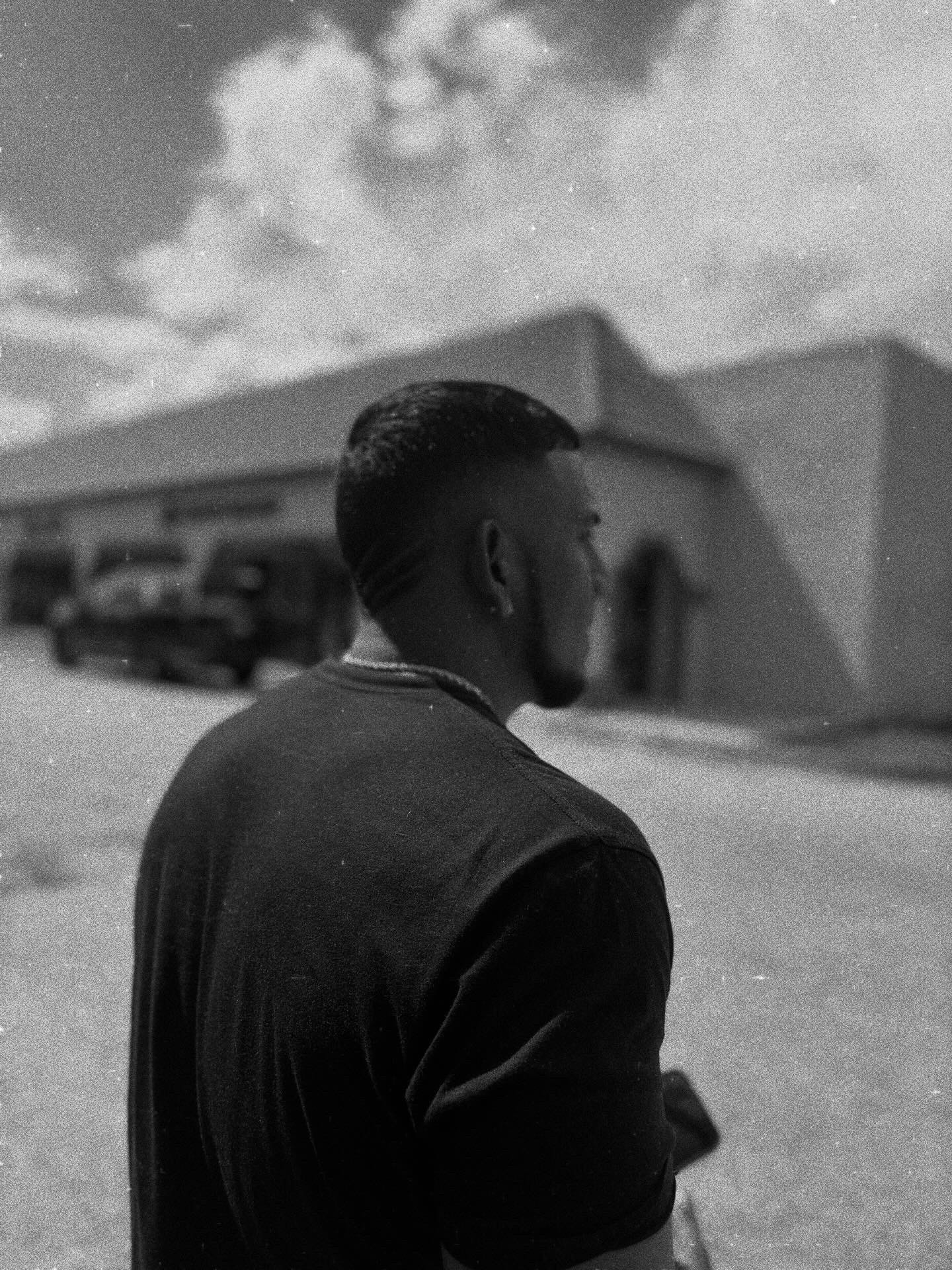 Side view of a person with short hair and beard, wearing a dark jacket, standing outdoors near a building.