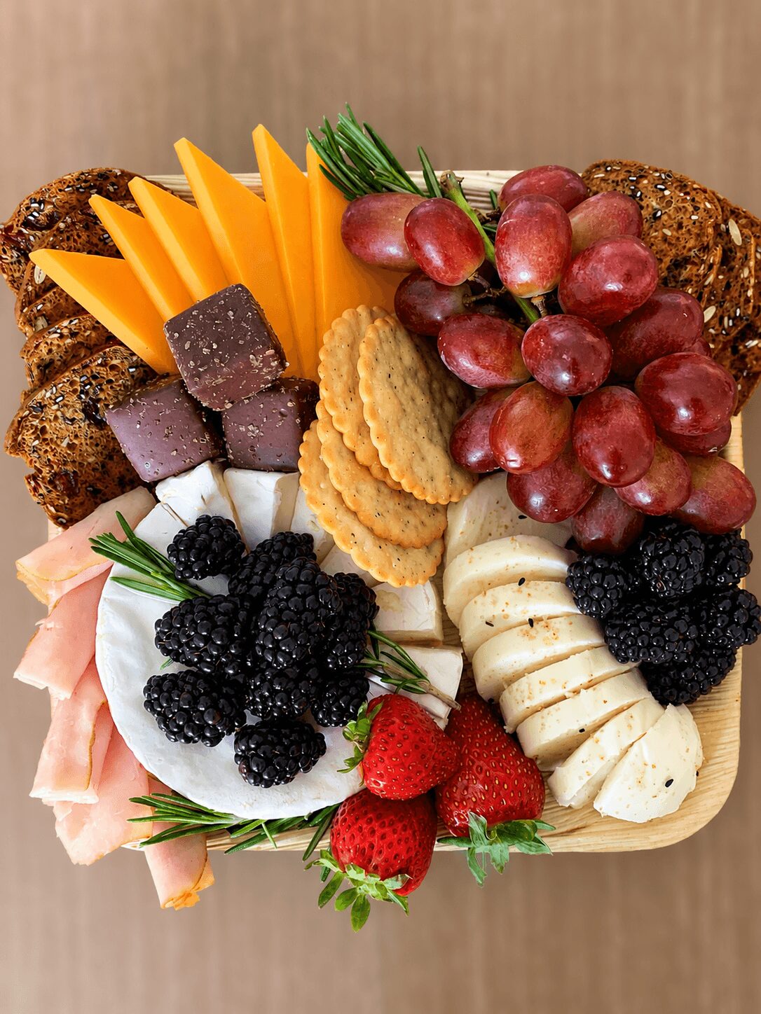 Cheese, grapes, strawberries, crackers, and assorted meats on a wooden platter.