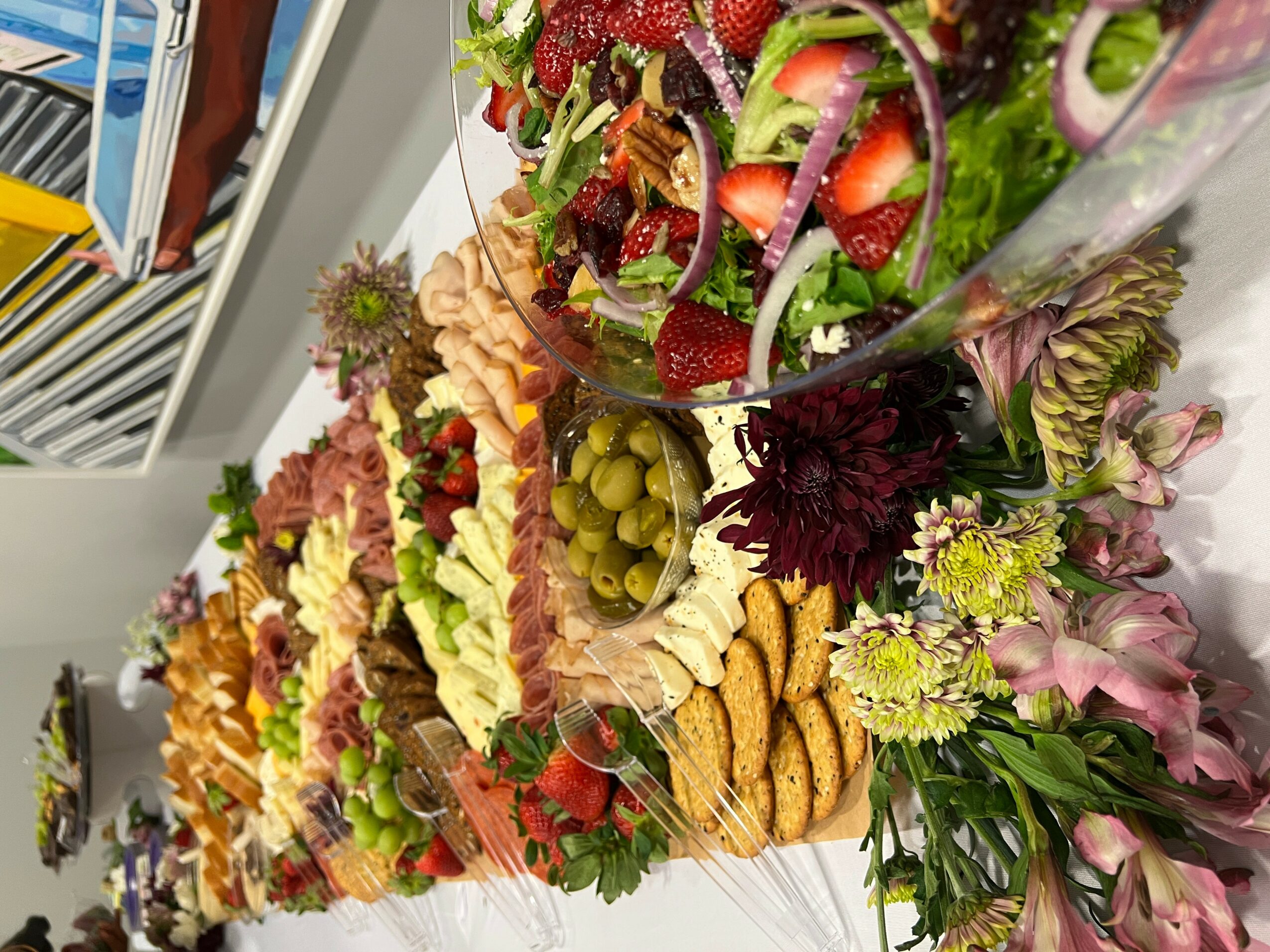 Assorted colorful salads and snacks arranged on a table with flowers and grapes, viewed from the side.