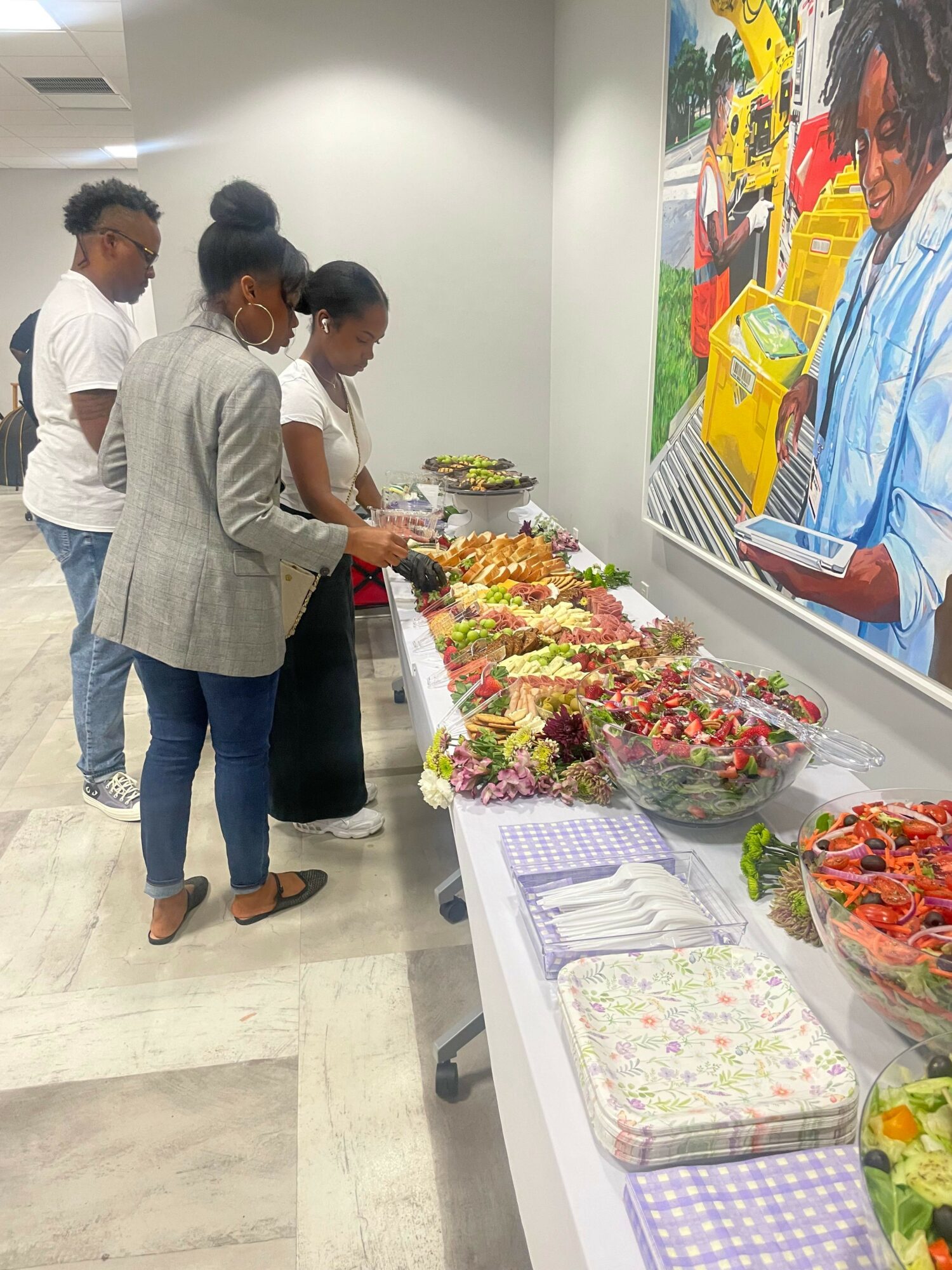 People browsing colorful flowers and gift items on a table in a store, with a large colorful poster on the wall.