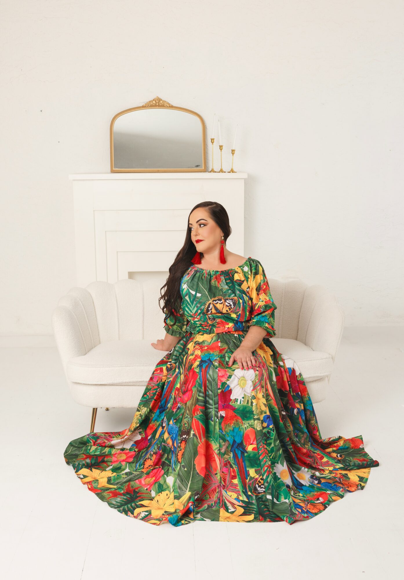 Woman in colorful dress sitting on a white sofa in a minimalistic room with a mirror and candles on a mantelpiece