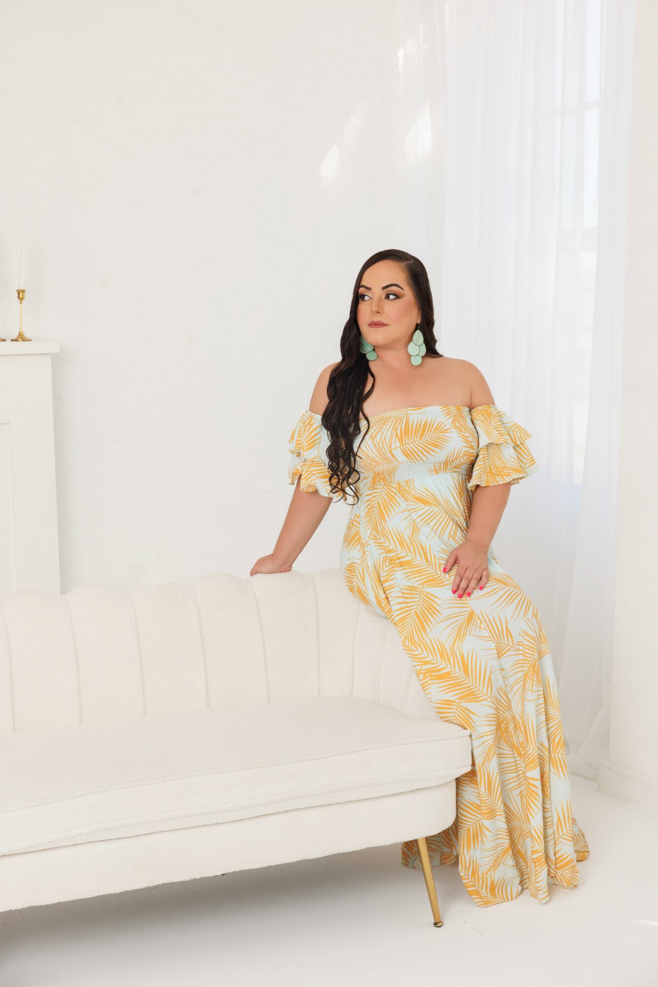 Woman in yellow and white dress sitting on a white sofa in a bright room with white curtains